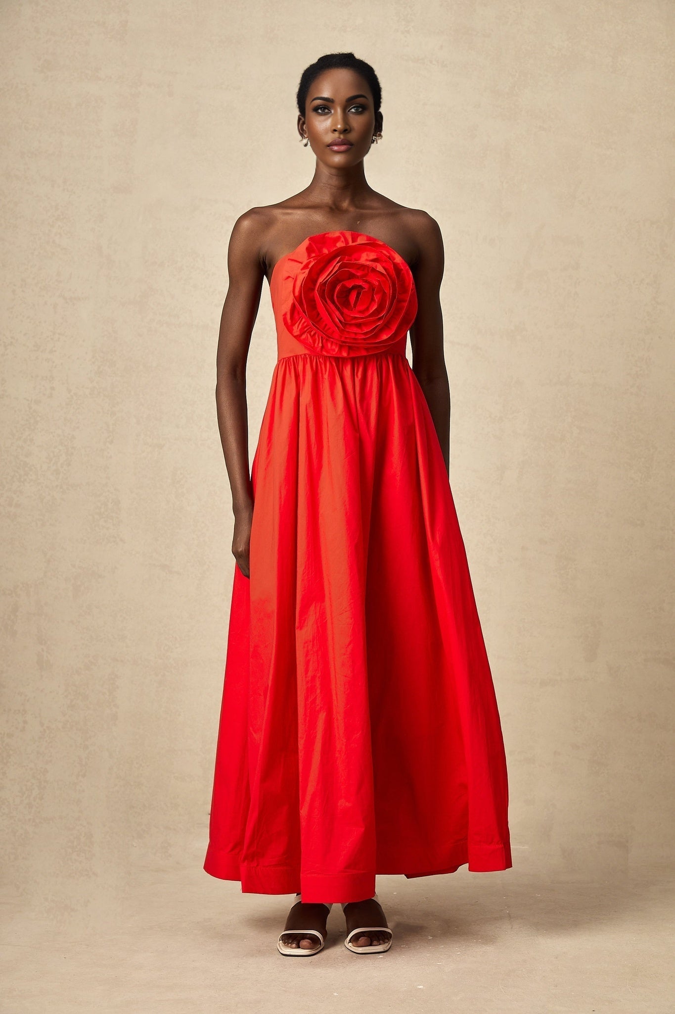 A woman wearing a long red maxi dress with ruffled 3d petal details
