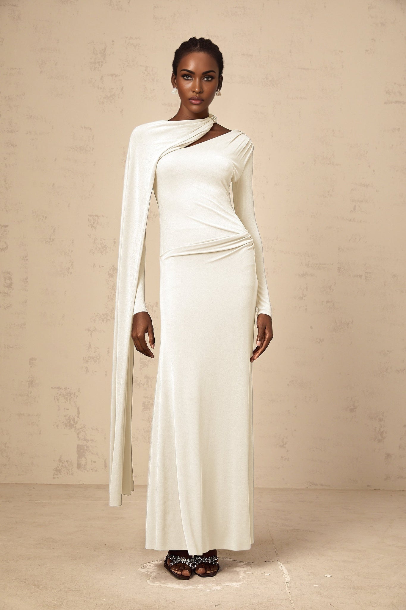A woman wearing a long white fitted maxi dress with a diagonal shawl detail across the bodice