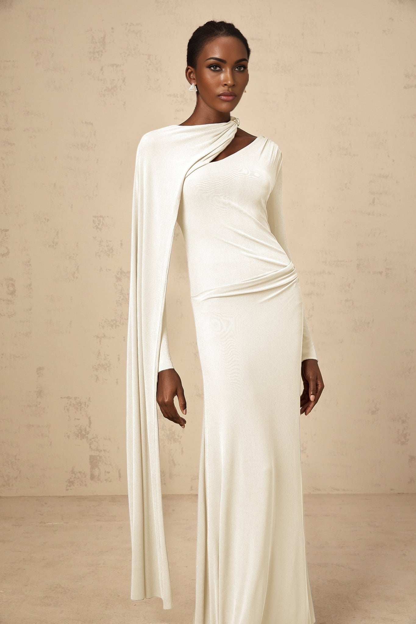 A woman wearing a long white fitted maxi dress with a diagonal shawl detail across the bodice