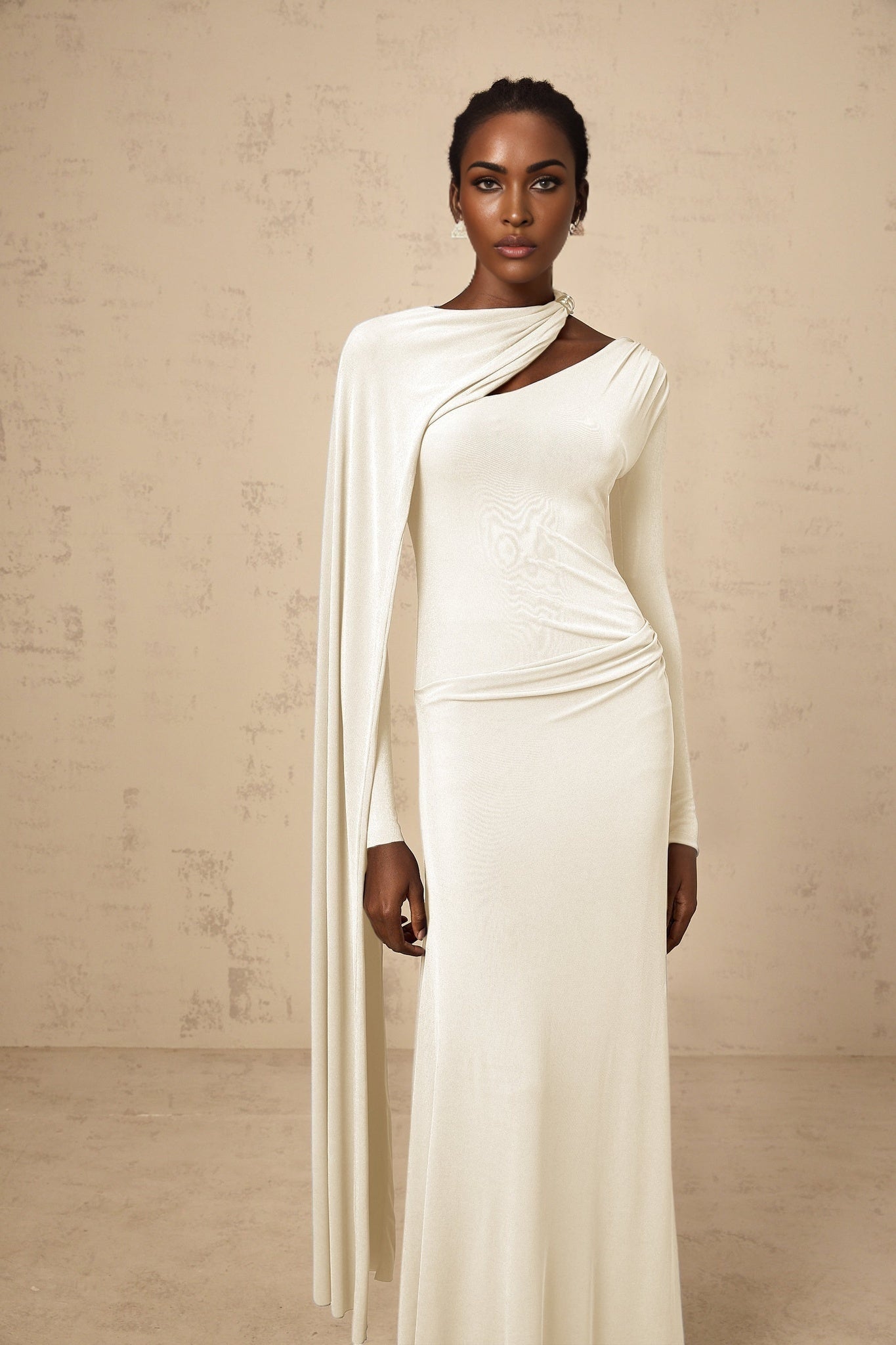 A woman wearing a long white fitted maxi dress with a diagonal shawl neckline