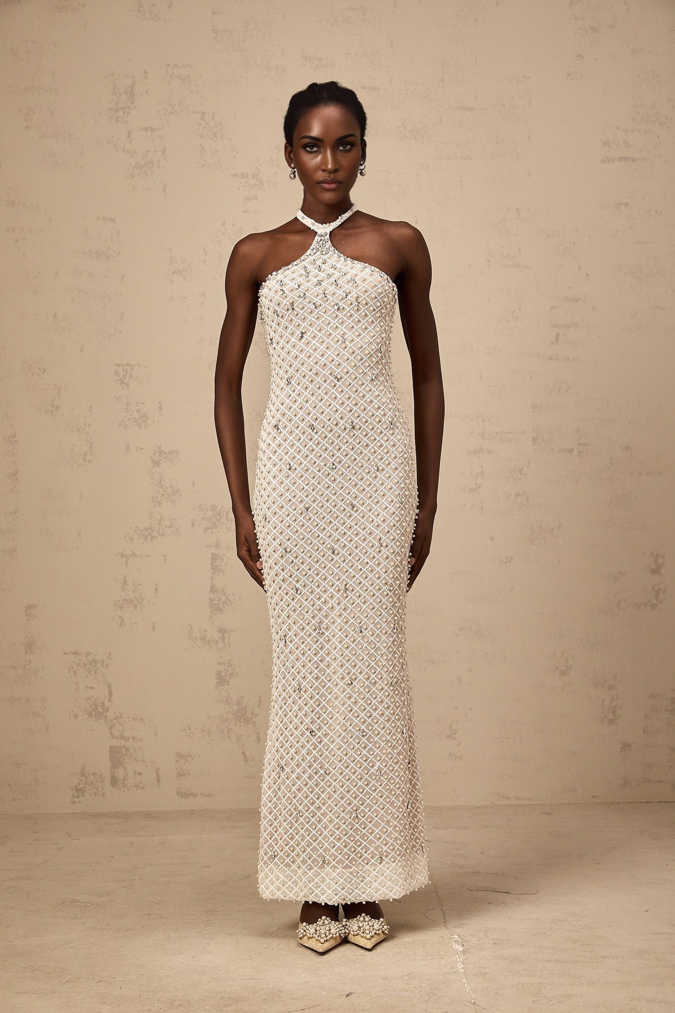 A woman wearing a long white halterneck maxi dress with embellishments standing against a plain background