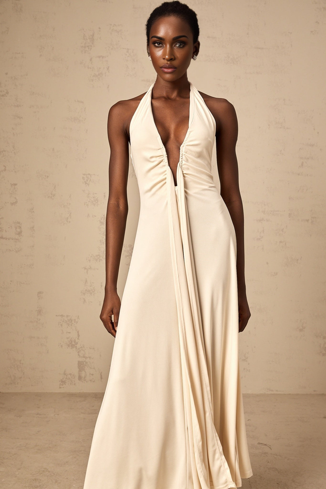 A woman wearing a long white maxi dress with a deep V neckline and draped fabric details