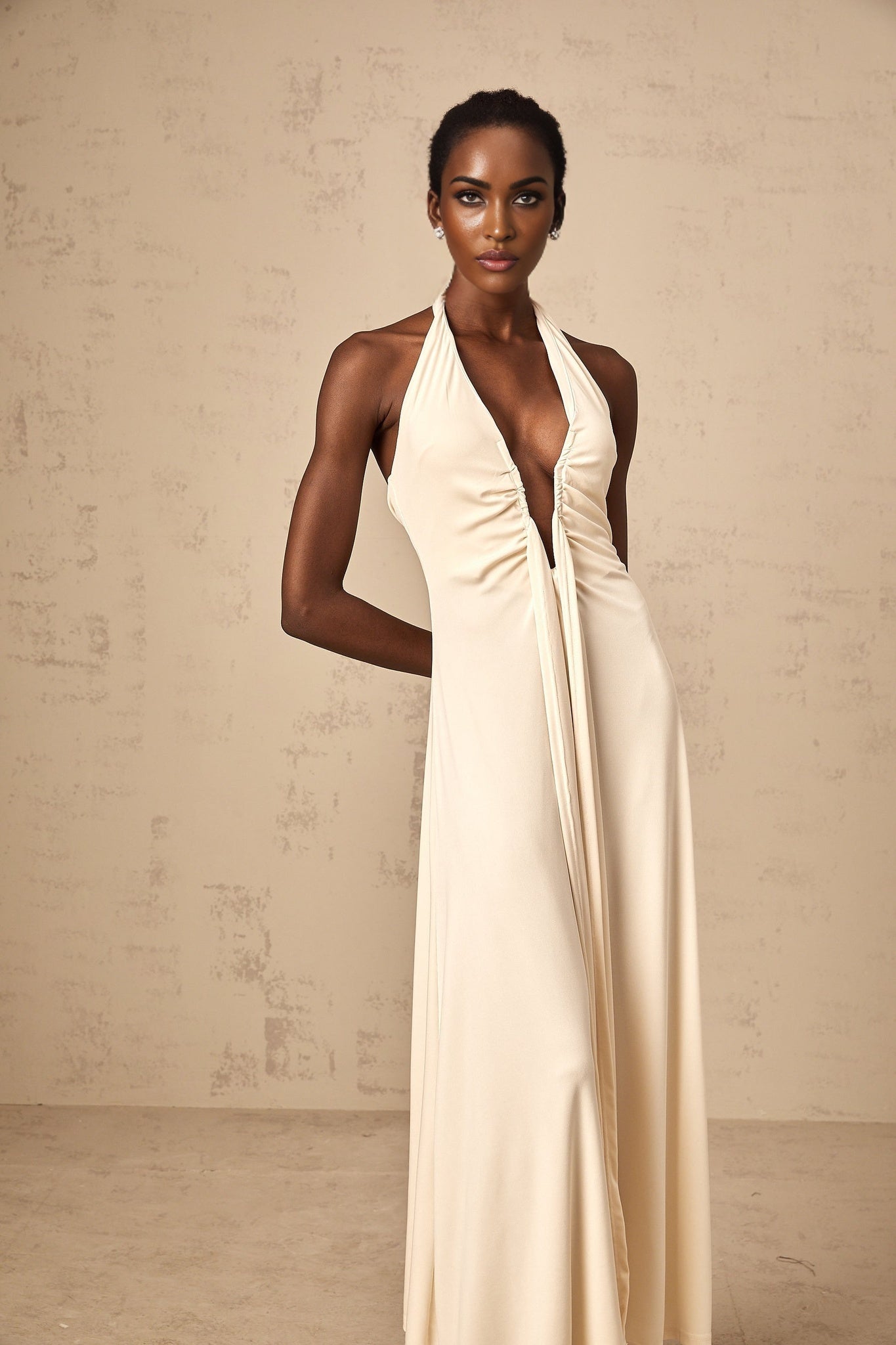 A woman wearing a long white maxi dress with a deep V neckline and draped fabric details