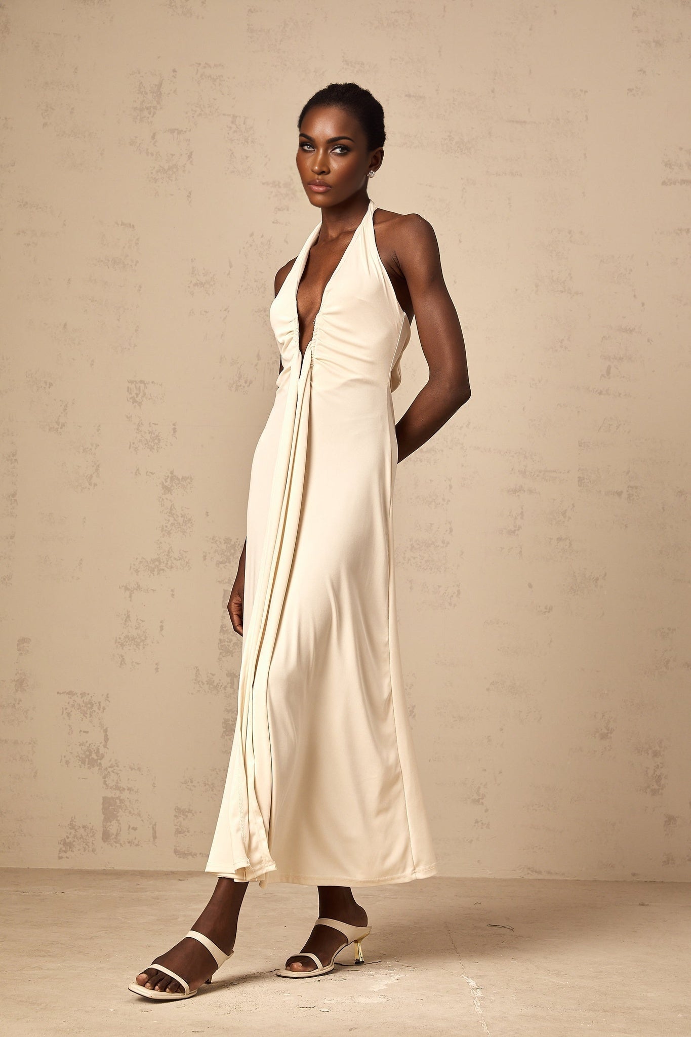 A woman wearing a long white maxi dress with a deep V neckline and draped fabric details