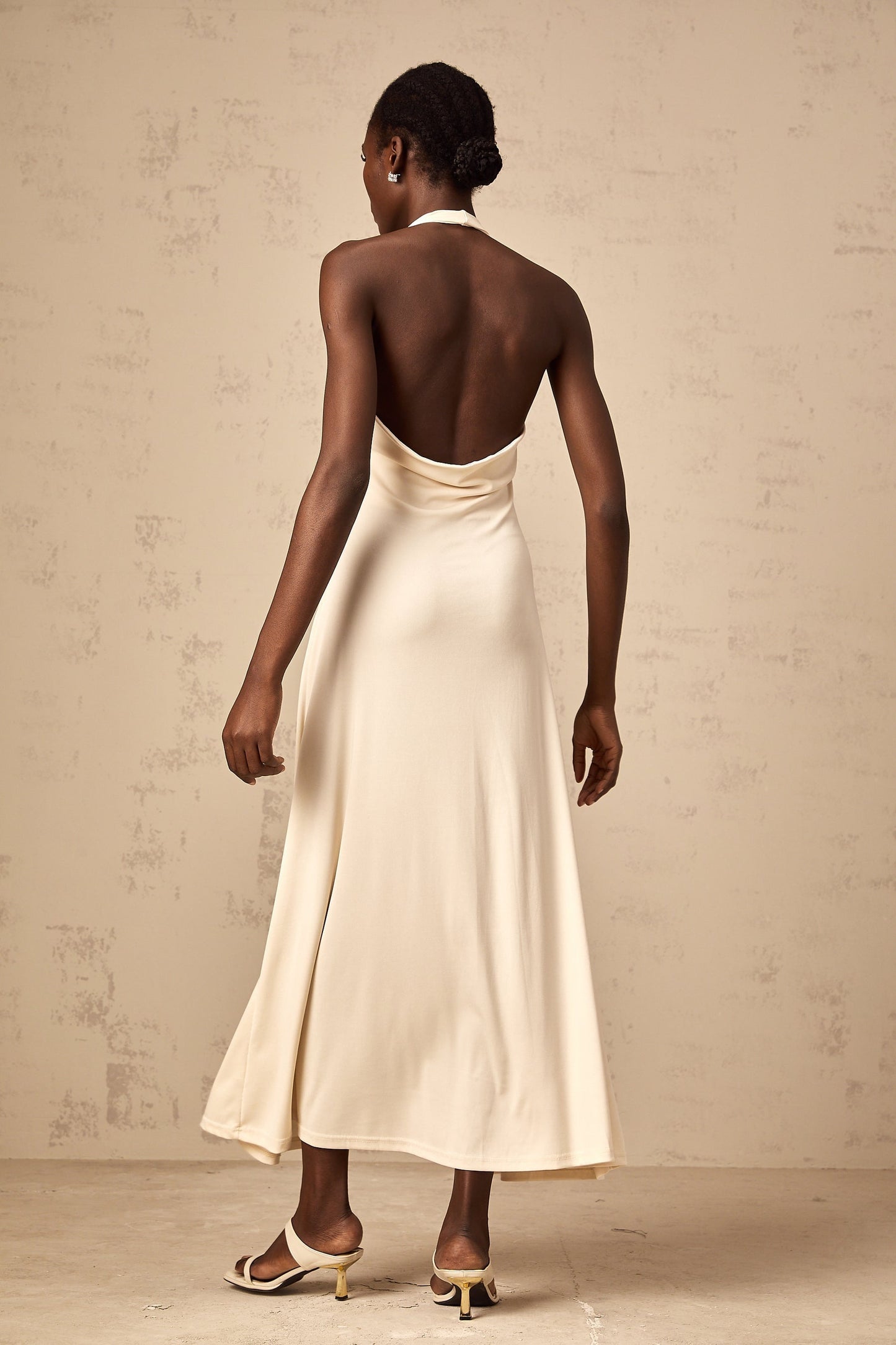 A woman wearing a long white maxi dress with a deep V neckline and draped fabric flowing to the floor