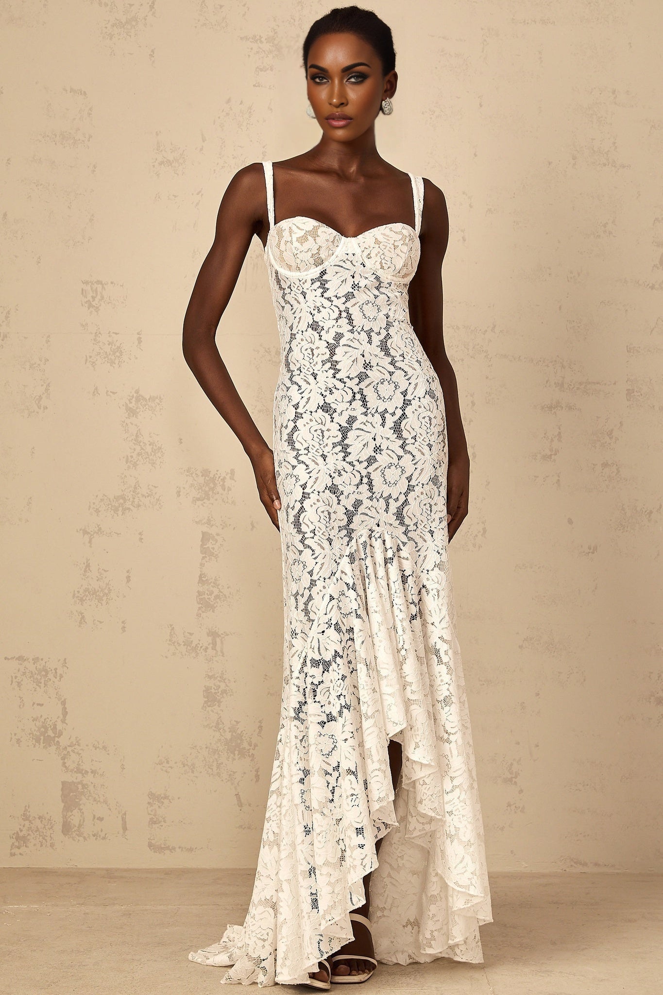A woman wearing a long white maxi dress with floral lace detailing and a bustier style bodice