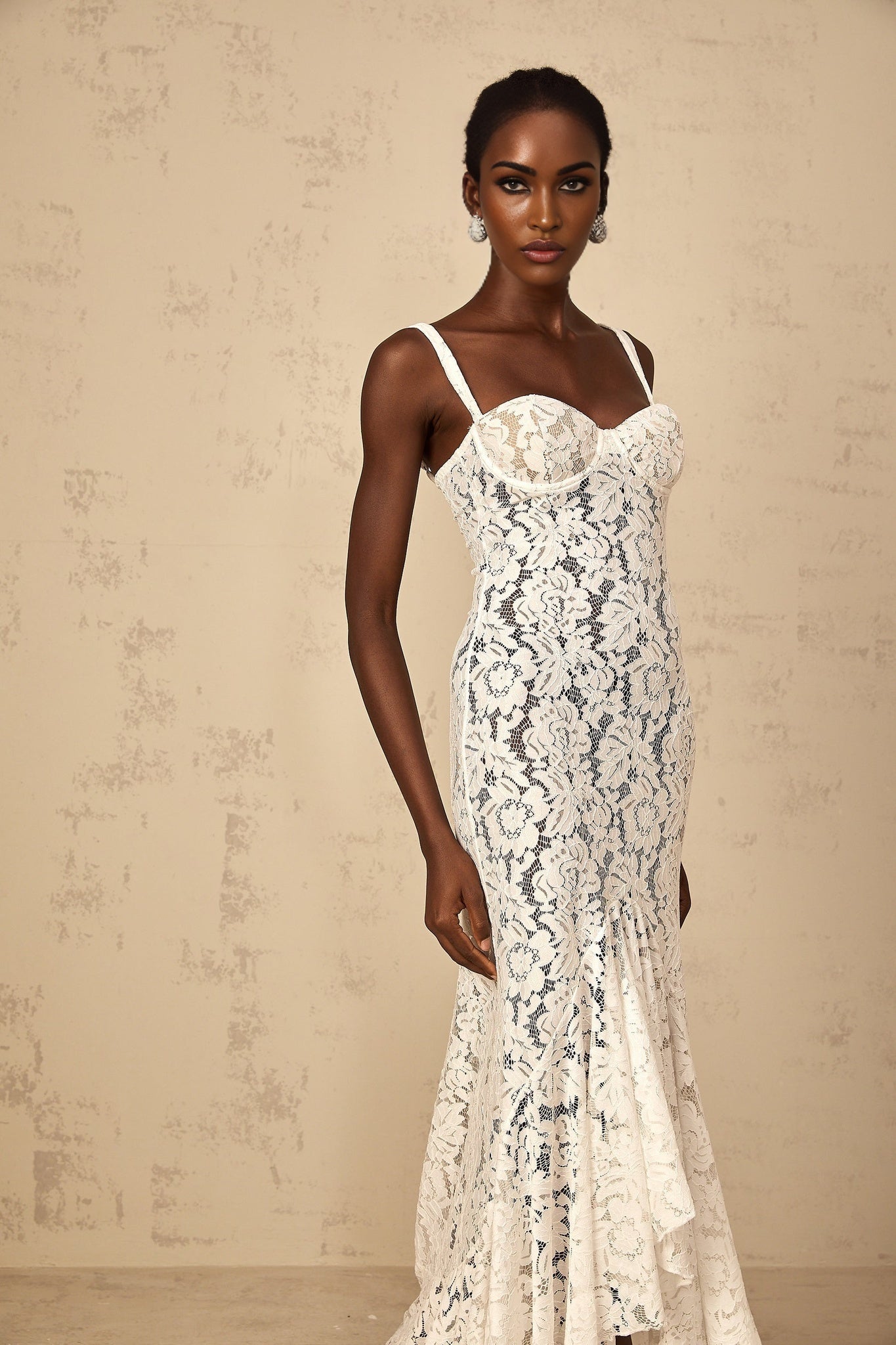 A woman wearing a long white maxi dress with floral lace detailing and a bustier style top