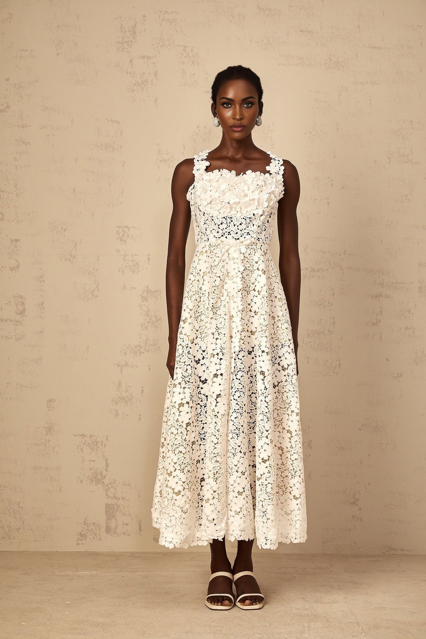 A woman wearing a long white maxi dress with shirred detailing and corded lace pattern standing in a relaxed pose