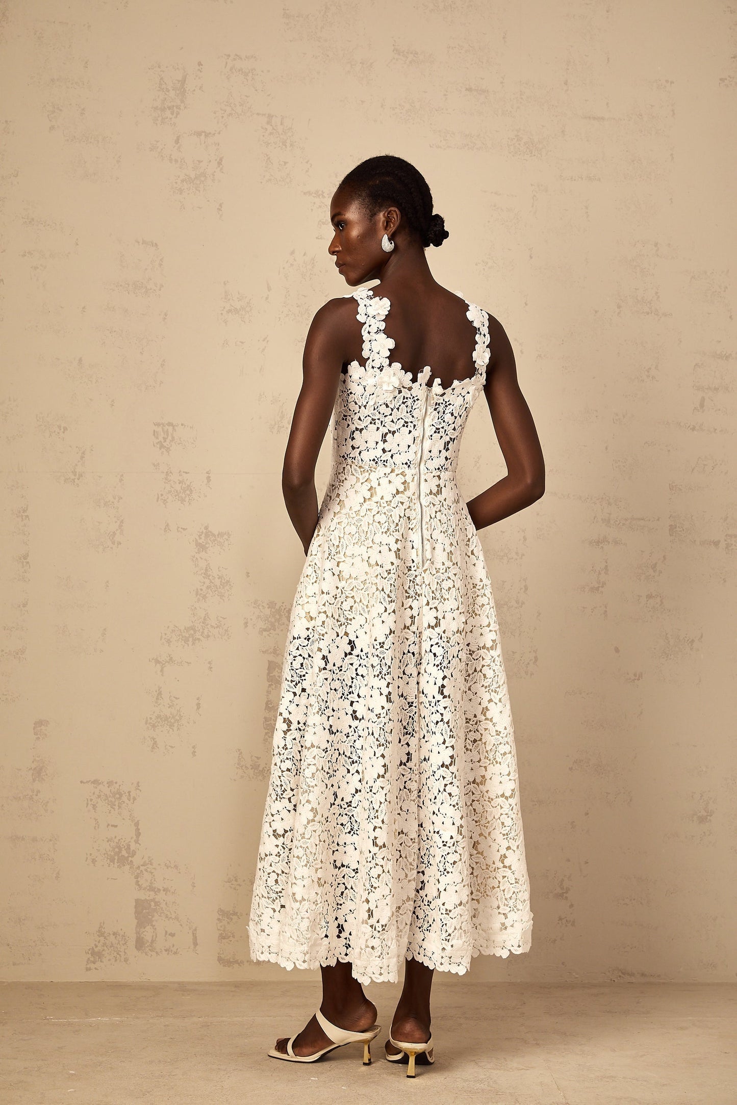 A woman wearing a long white maxi dress with shirred detailing and corded lace patterns standing in a relaxed pose