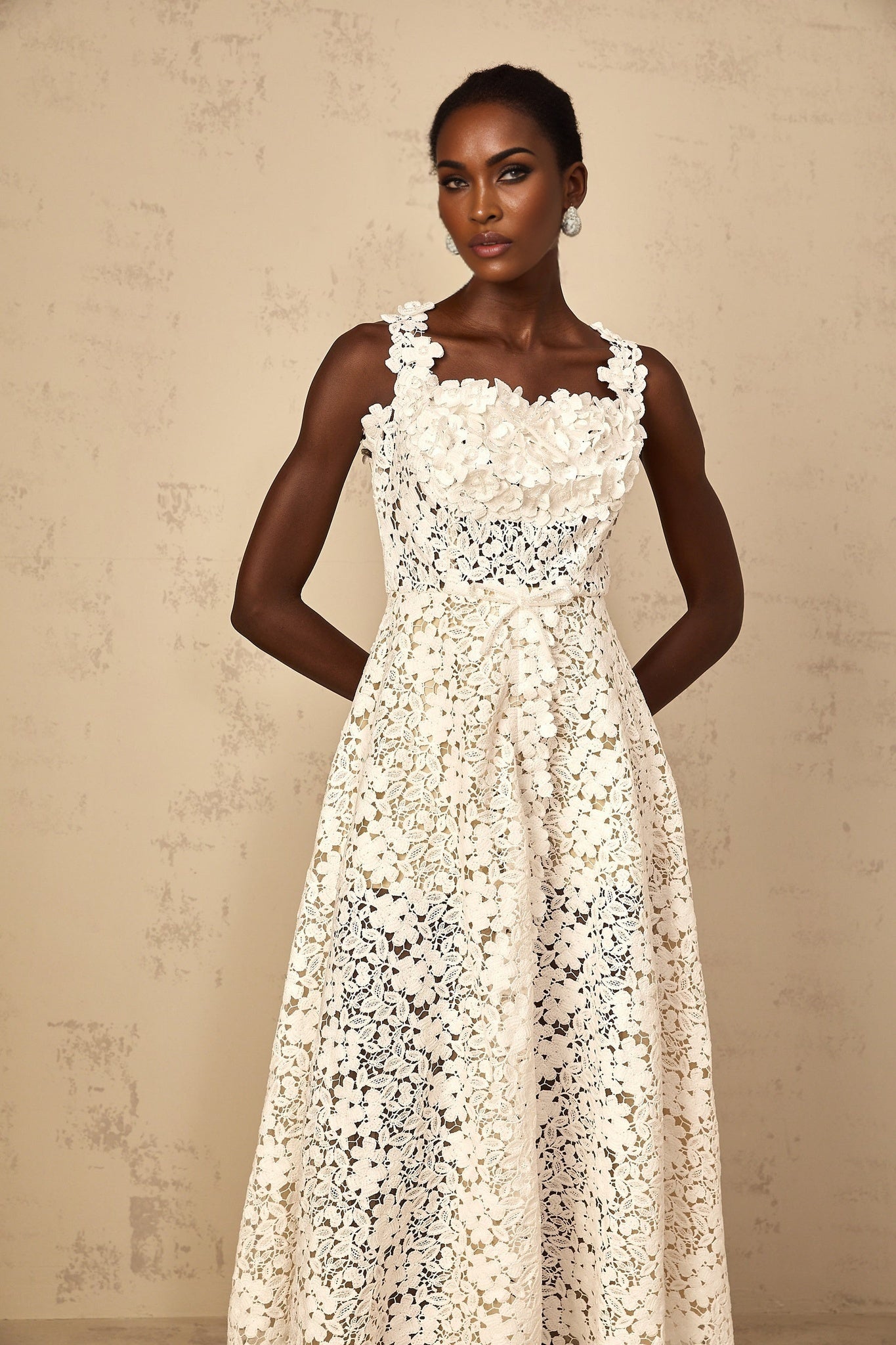 A woman wearing a long white maxi dress with shirred detailing and corded lace patterns standing in a relaxed pose