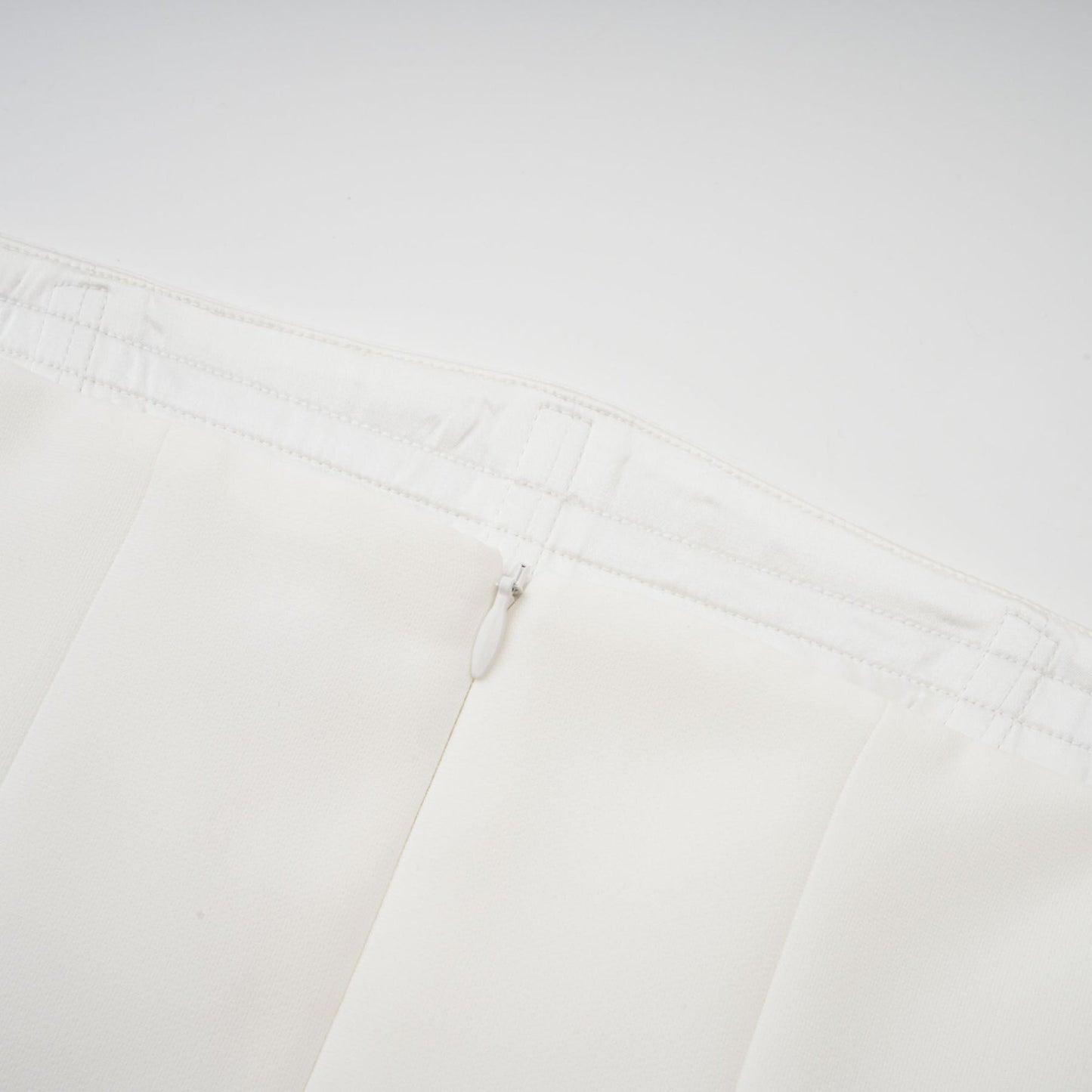 A woman wearing a long white pleated maxi dress with an offshoulder neckline