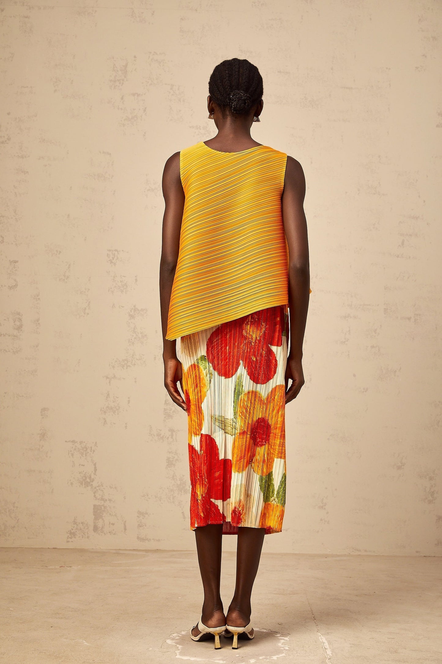 A woman wearing a matching amberorange top and skirt set with a crinkled texture The top is sleeveless and the skirt falls to mid length The outfit has a vibrant summery appearance