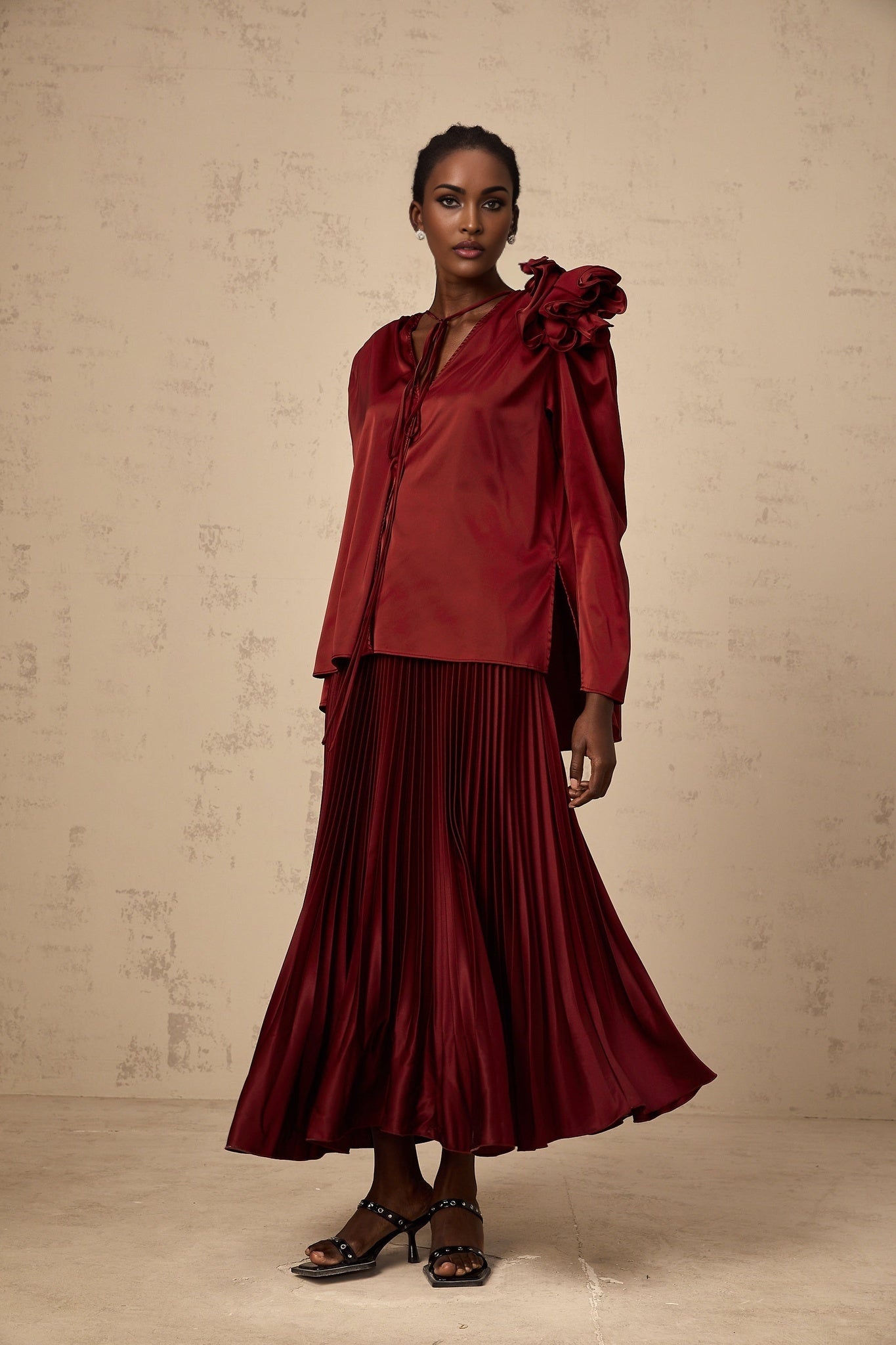 A woman wearing a matching blouse and skirt set in satin fabric with flower appliques The top is a sleeveless blouse and the skirt is knee length Both pieces feature delicate floral embellishments