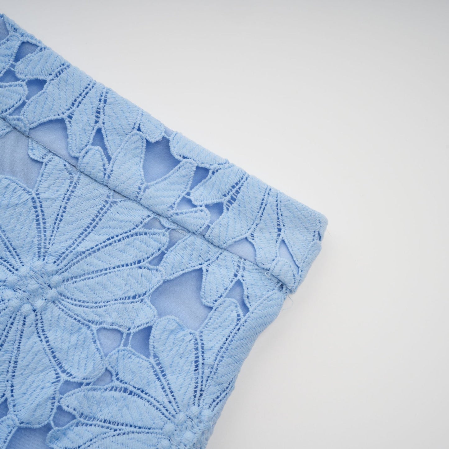 A woman wearing a matching blue lace top and skirt set The top is sleeveless with a high neck and the skirt is knee length Both pieces feature an intricate floral guipure lace pattern