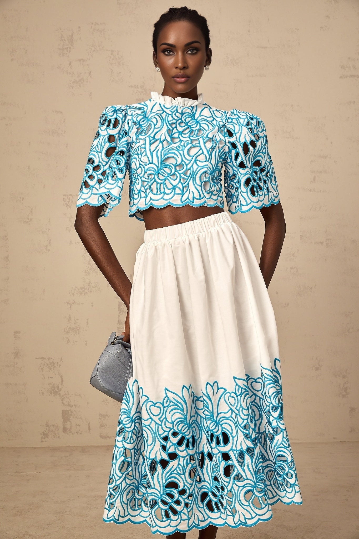 A woman wearing a matching blue twopiece outfit consisting of a top and skirt The top features cutout details and embroidery The set has a delicate and feminine appearance