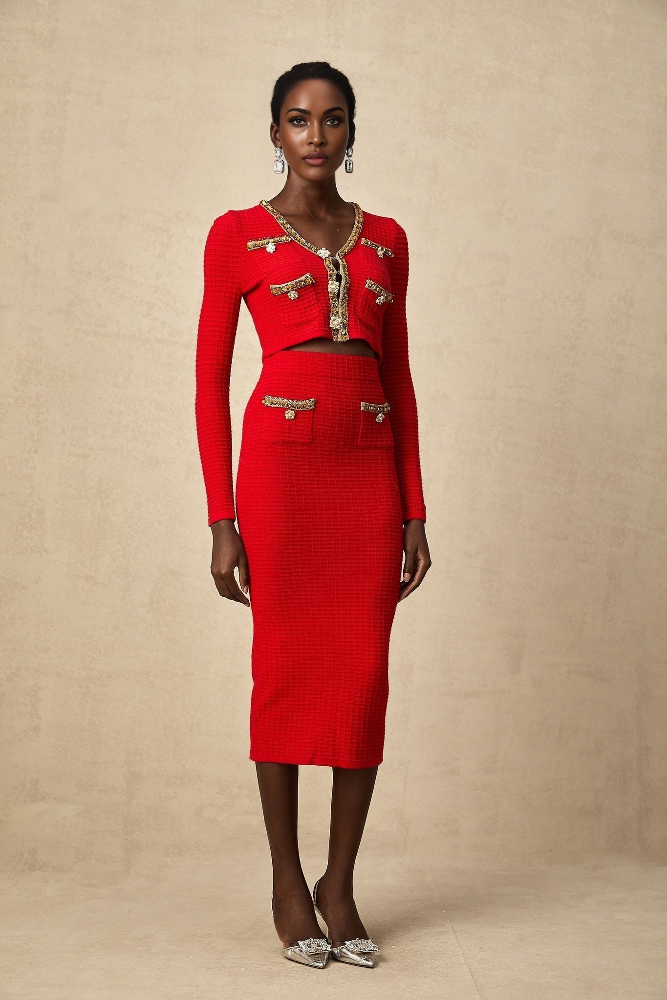 A woman wearing a matching red knitted cardigan and skirt set The cardigan features embellishments and the outfit is called Axelle