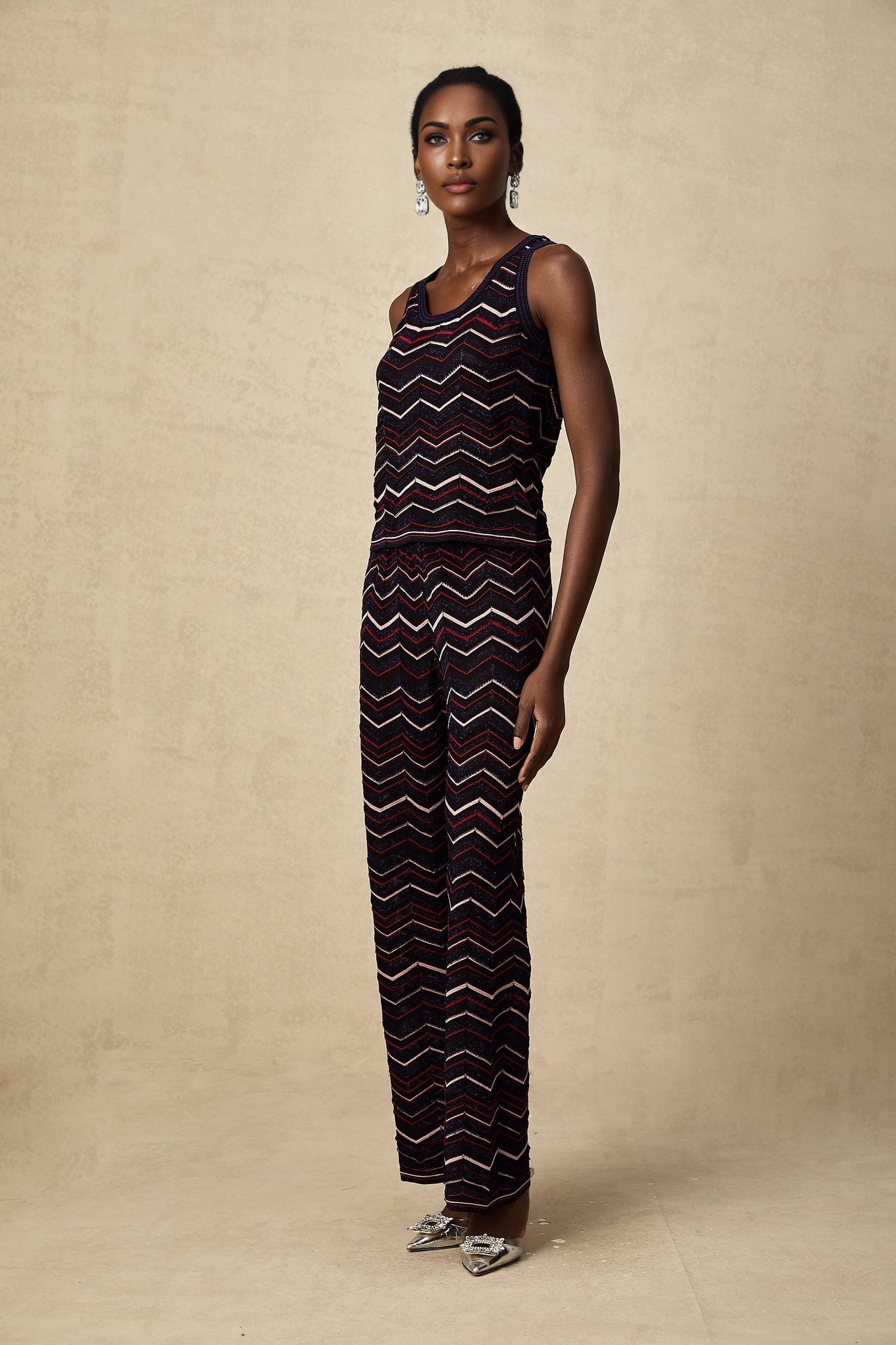 A woman wearing a matching set consisting of a crochet knit top and trousers with a zigzag pattern in a light color The top has short sleeves and the trousers are wide legged