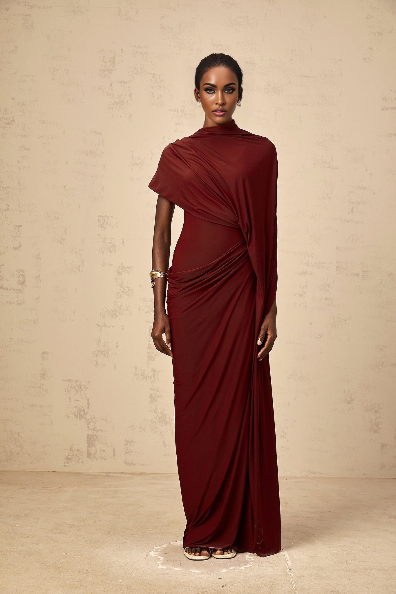 A woman wearing a matching set consisting of an asymmetrical draped cape and dress in a flowing fabric the cape drapes elegantly over one shoulder while the dress hugs the body