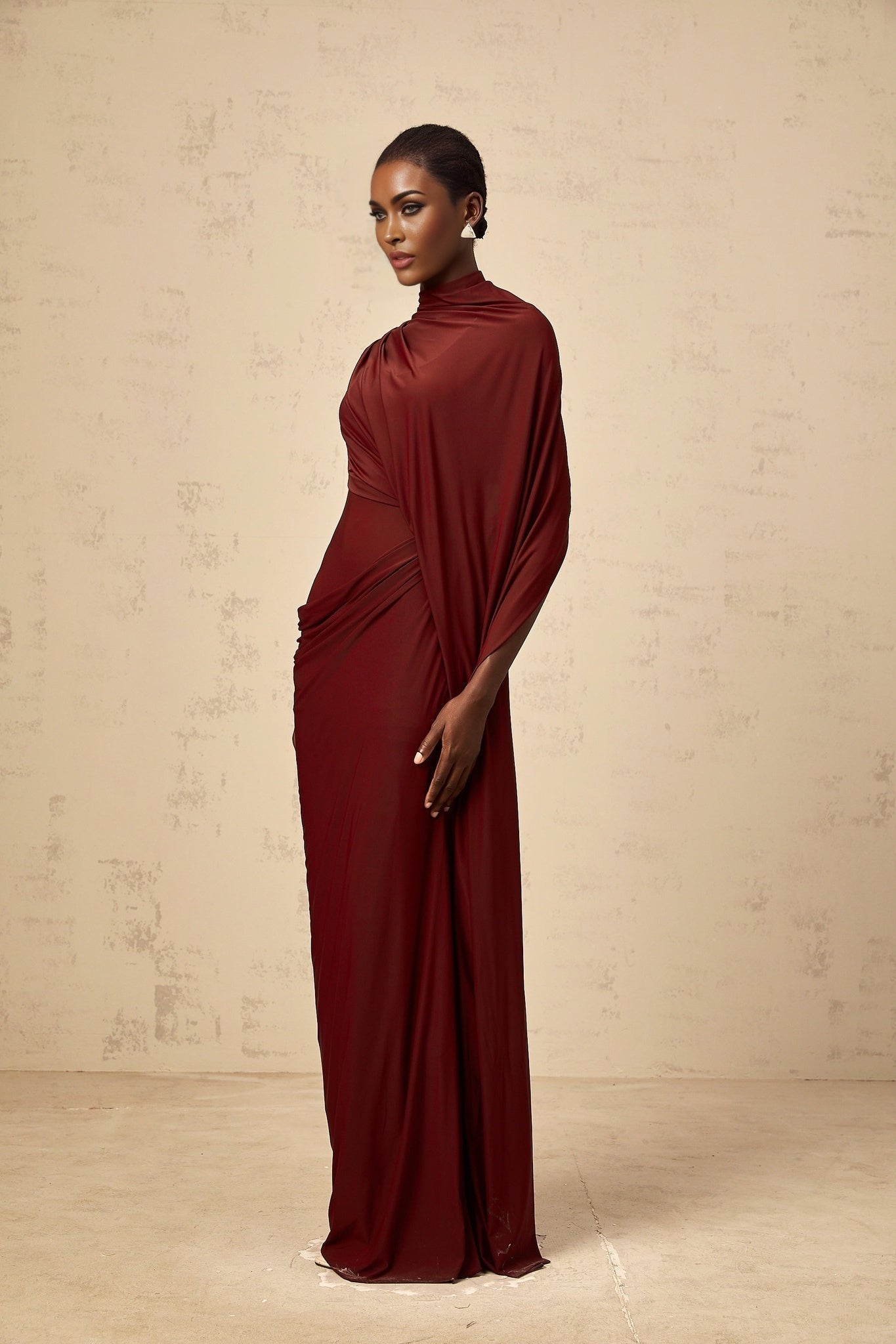 A woman wearing a matching set consisting of an asymmetrical draped cape and dress in a solid color The cape drapes elegantly over one shoulder while the dress features a sleek silhouette