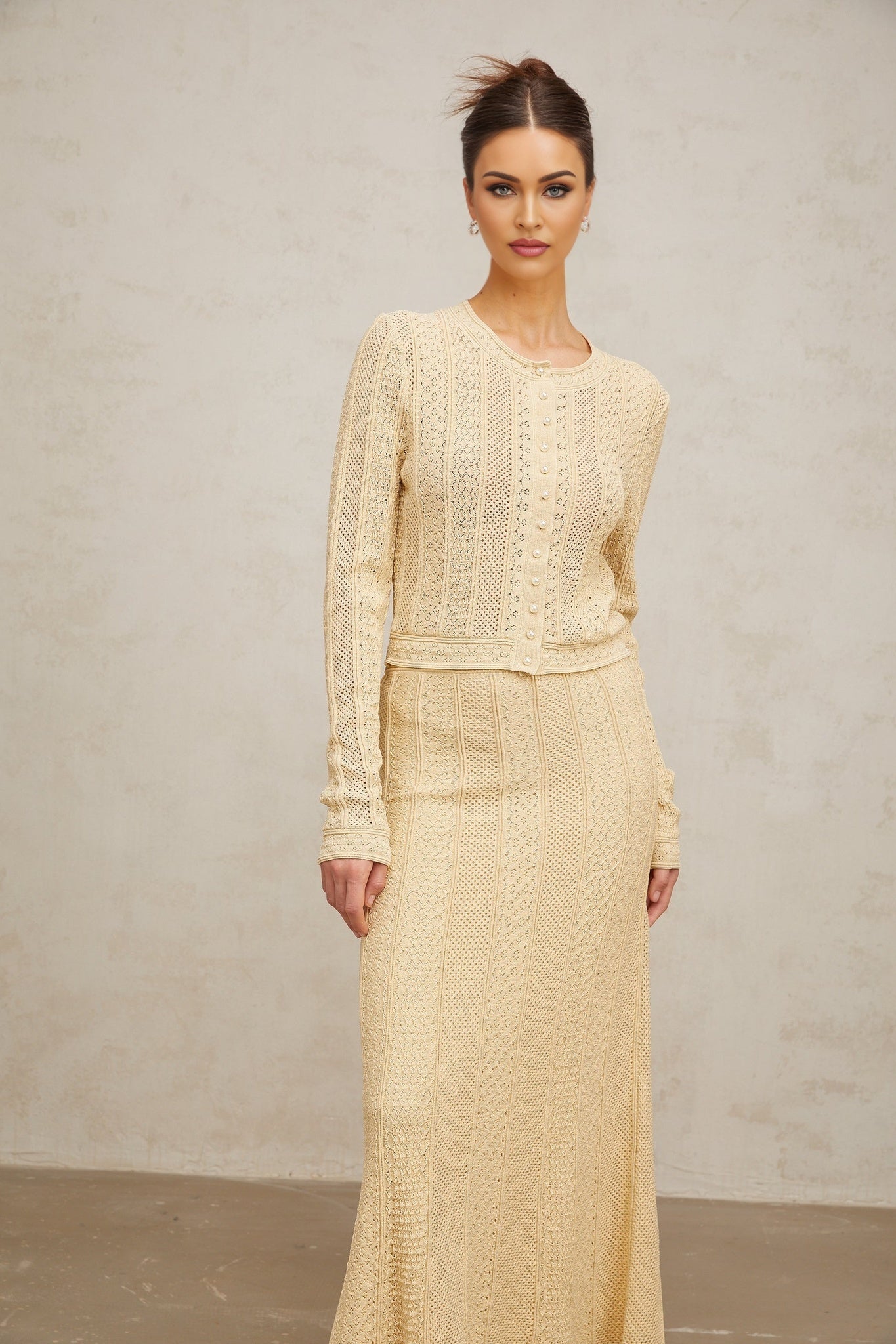 A woman wearing a matching white pointelle knit cardigan and skirt set The cardigan has long sleeves and an open front The skirt is knee length The outfit has a delicate lacy pattern throughout