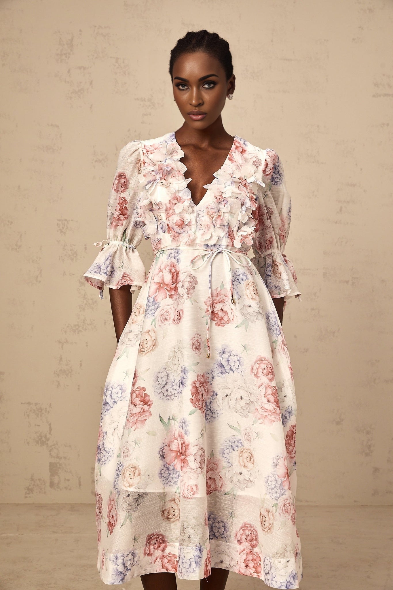 A woman wearing a midi dress with a vibrant three dimensional floral print featuring petal designs in various colors against a light background