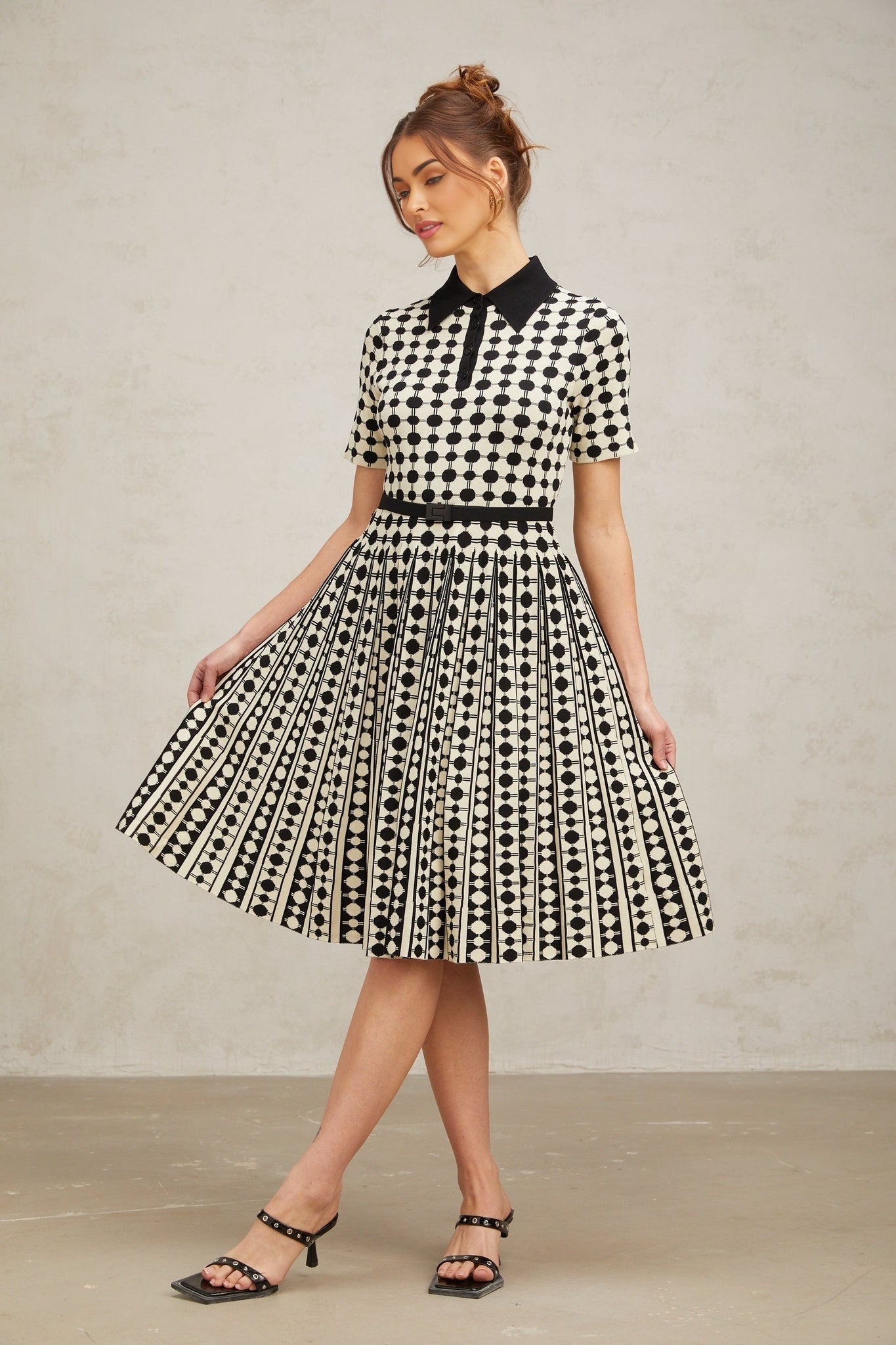 A woman wearing a midi length knit dress with color blocked sections and polka dot patterns in contrasting colors