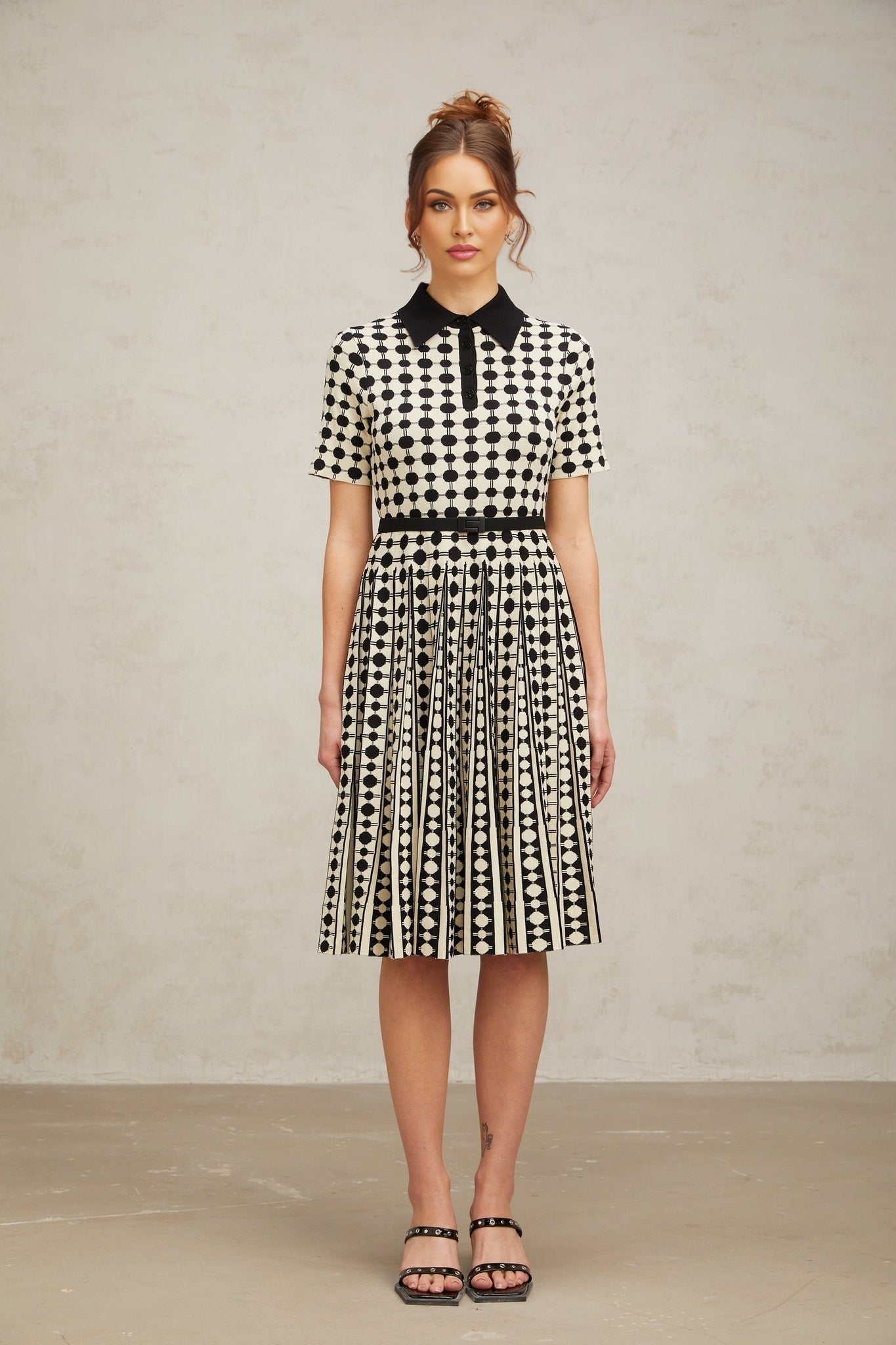A woman wearing a midi length knit dress with color blocked sections and polka dot patterns in contrasting colors