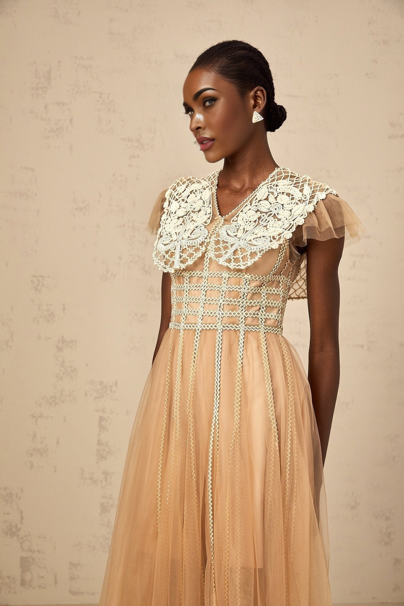 A woman wearing a midi length tulle dress in neutral tones with lace panel details