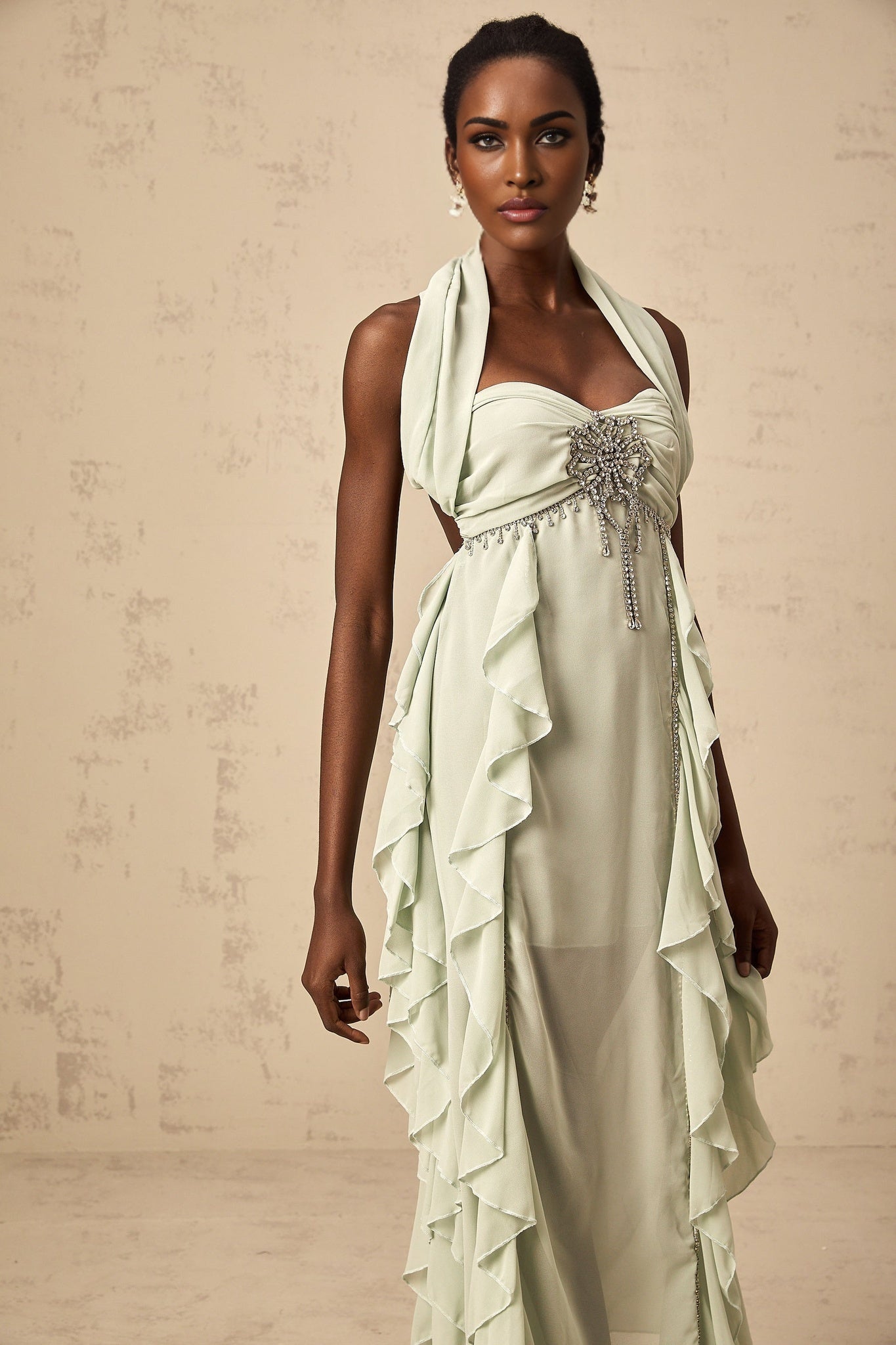 A woman wearing a midilength dress with ruffled details and embellishments standing in a neutral pose