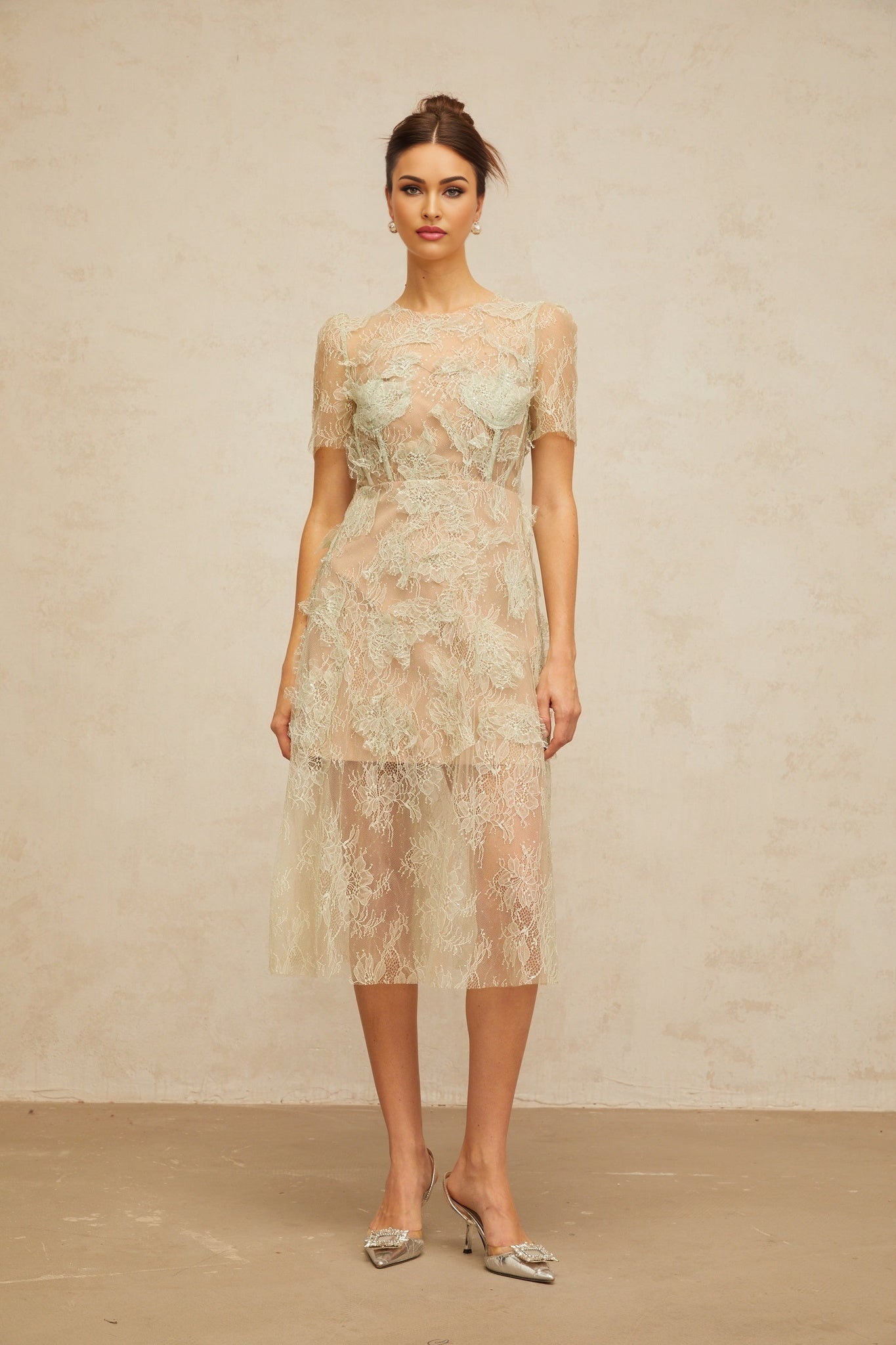 A woman wearing a mintgreen midi dress with floral lace pattern standing against a plain background