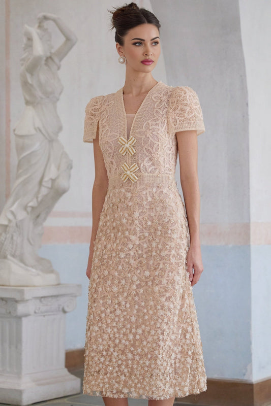 A woman wearing a neutral colored midi dress with crochet detailing and faux flower embellishments standing in a relaxed pose