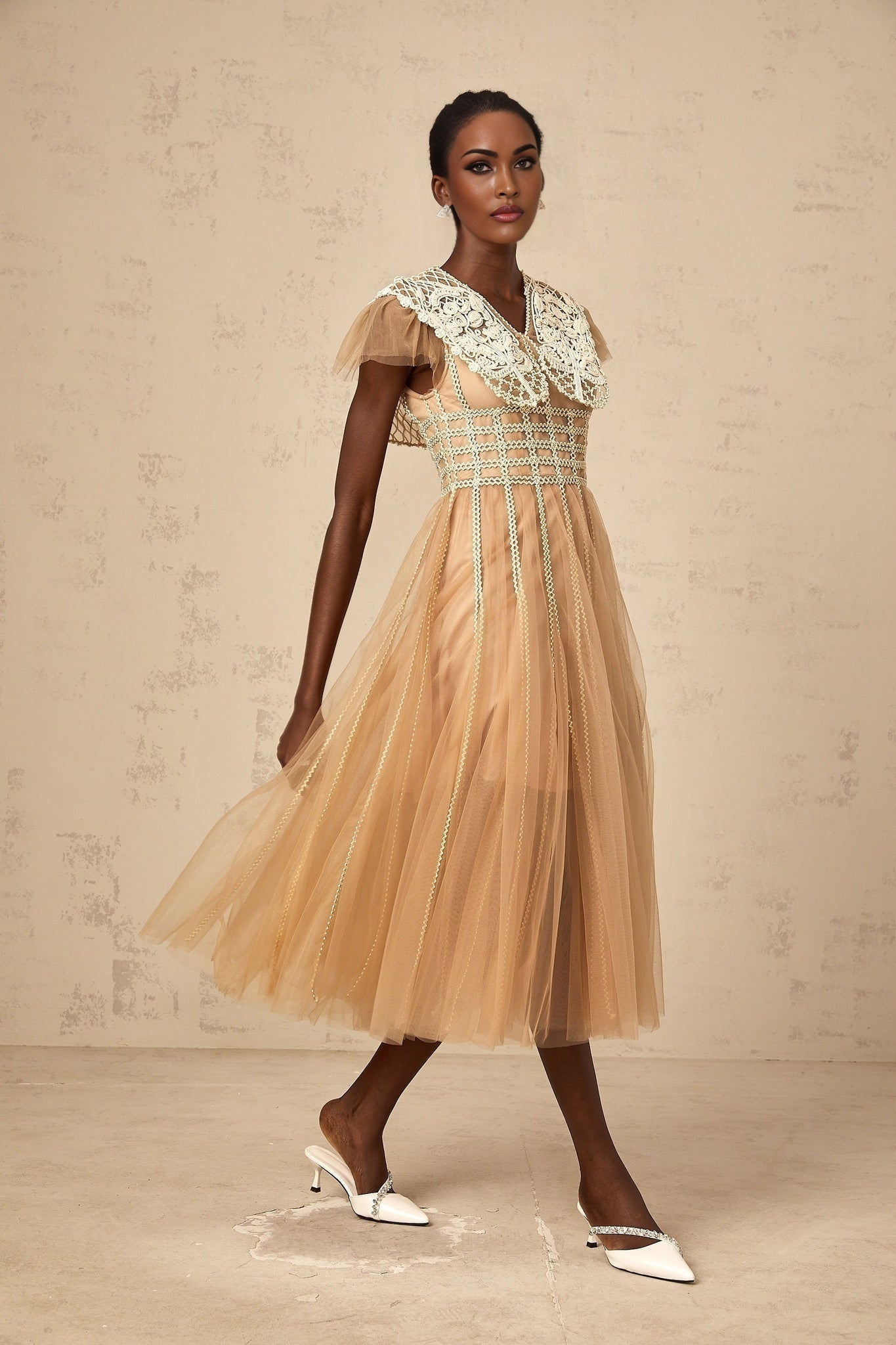 A woman wearing a neutral colored midi dress with lace panels and tulle details
