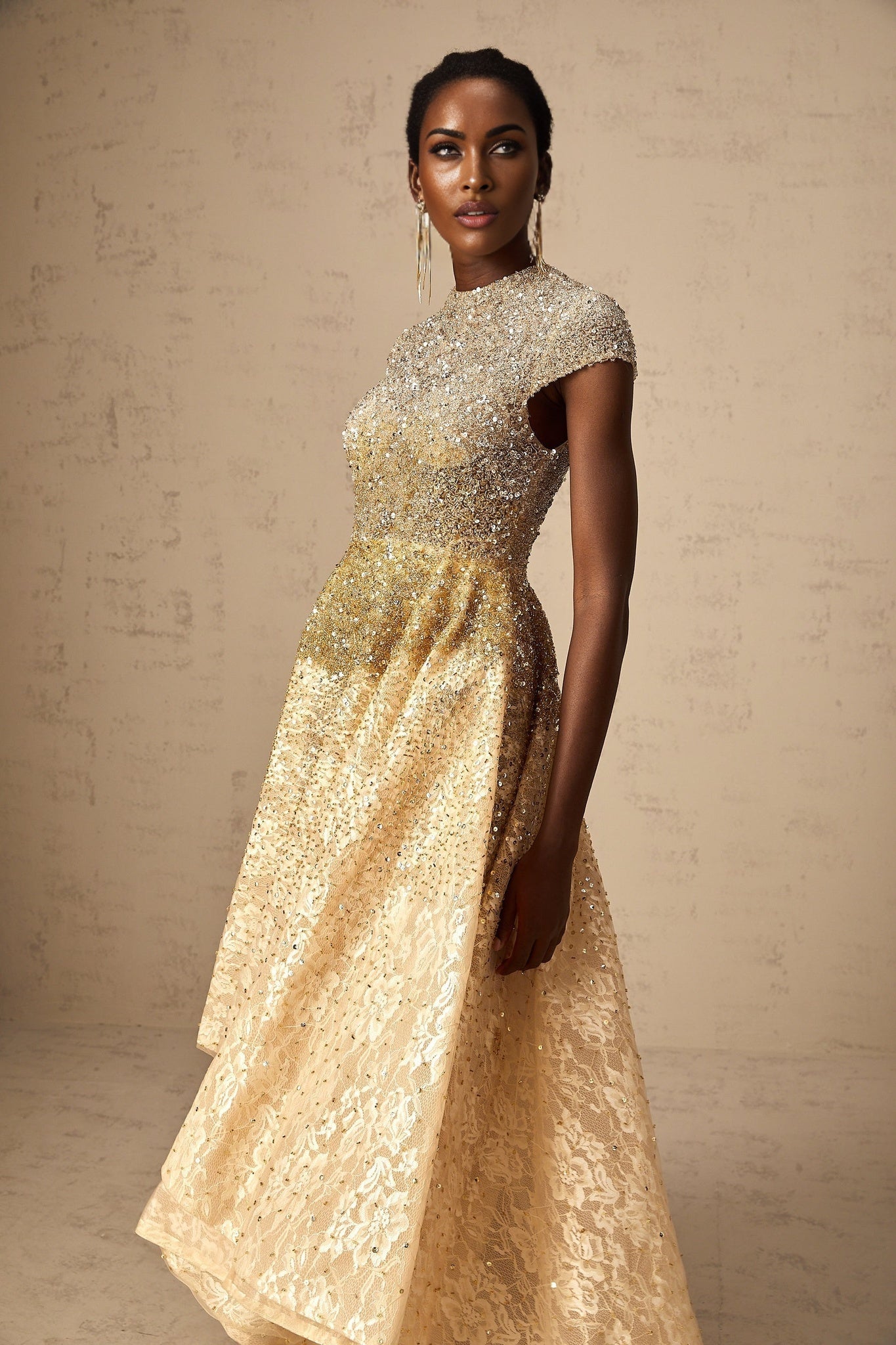 A woman wearing a neutral colored sequined dress with a high low hemline standing in a relaxed pose