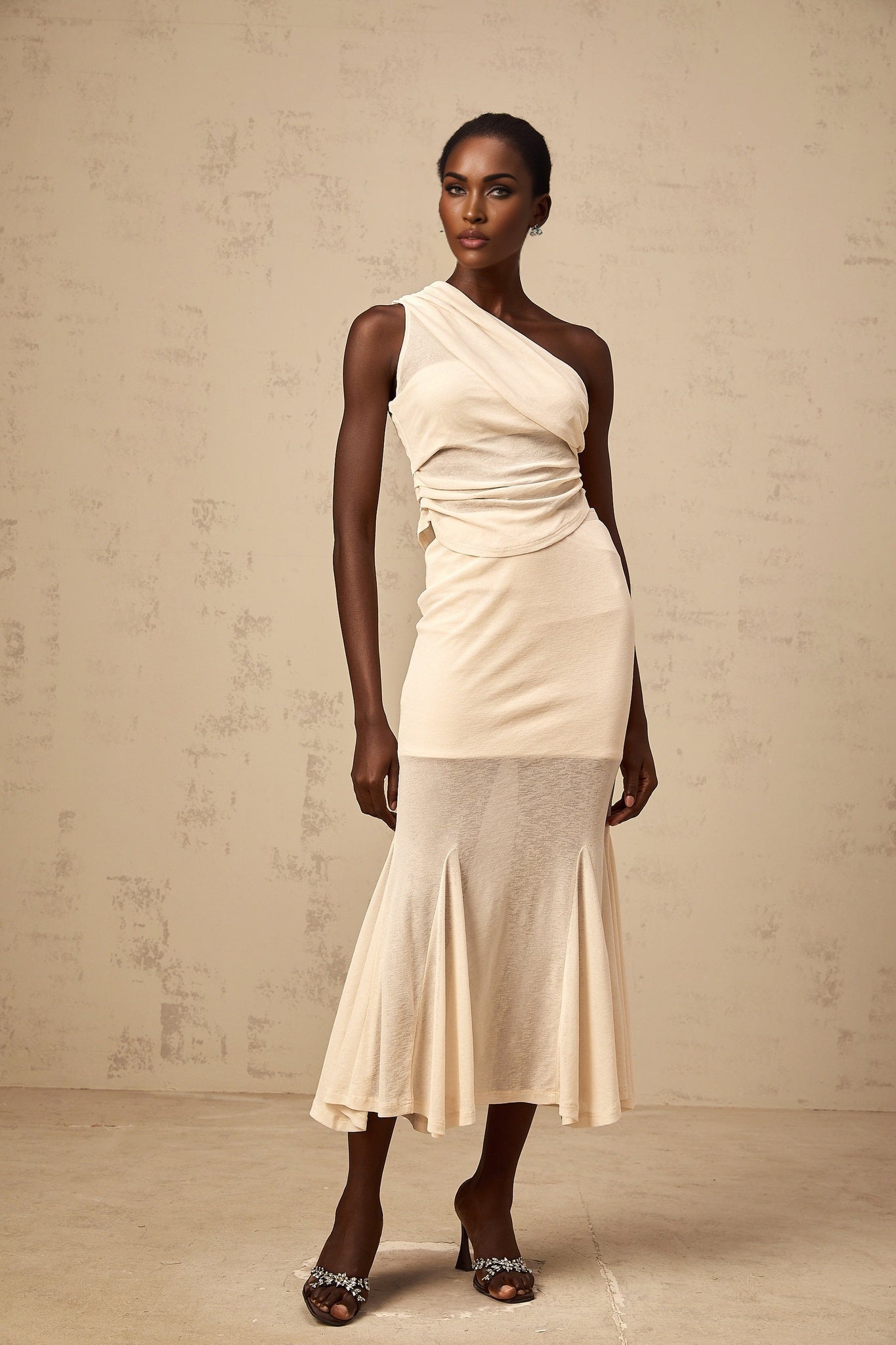 A woman wearing a neutralcolored matching set consisting of a ruched stretch top and skirt The outfit has a formfitting design with gathered fabric details