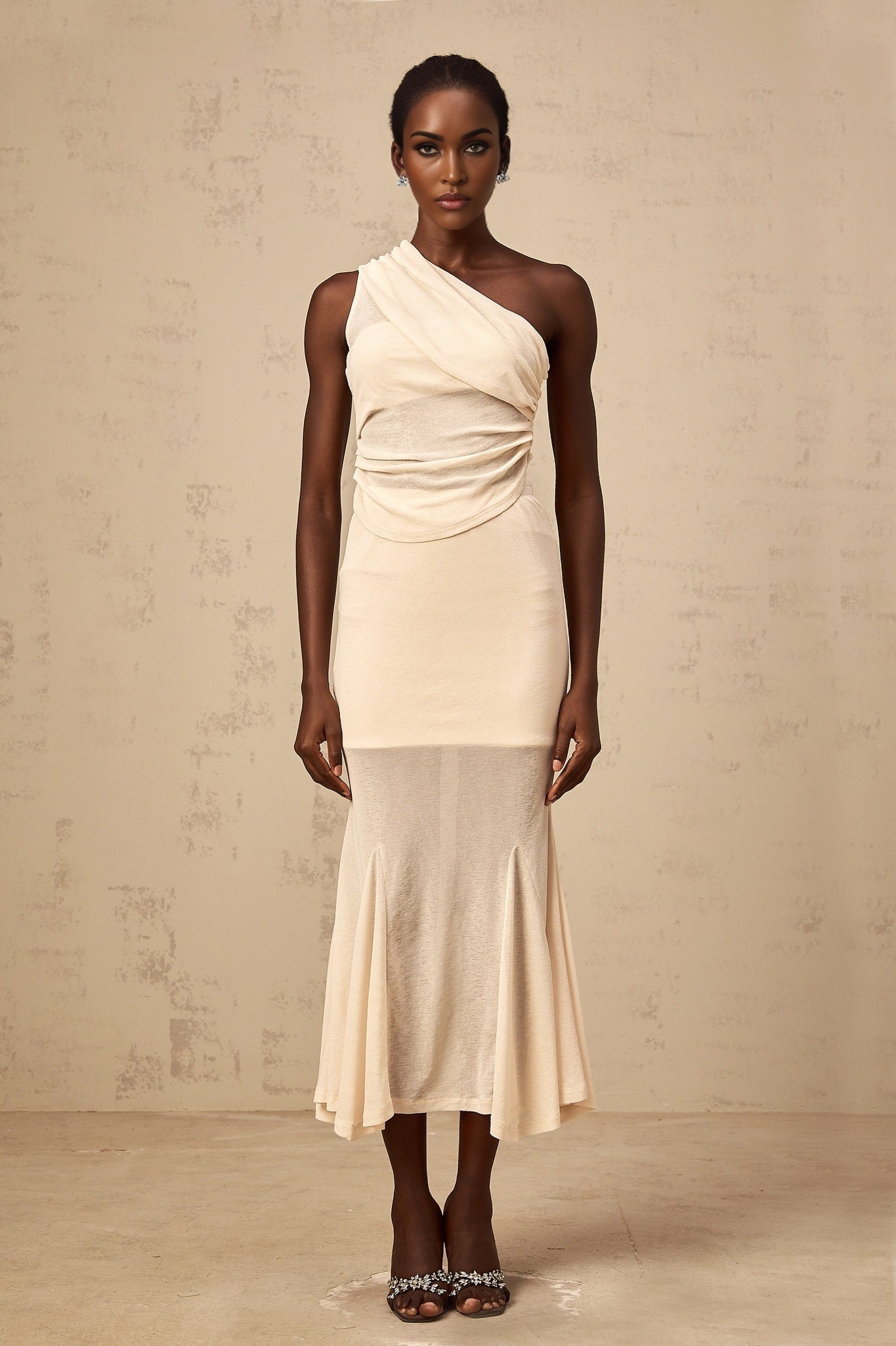 A woman wearing a neutralcolored matching set consisting of a ruched stretch top and skirt The top has long sleeves and the skirt is fitted The outfit is designed by Gwenaelle and showcases a stylish and comfortable look