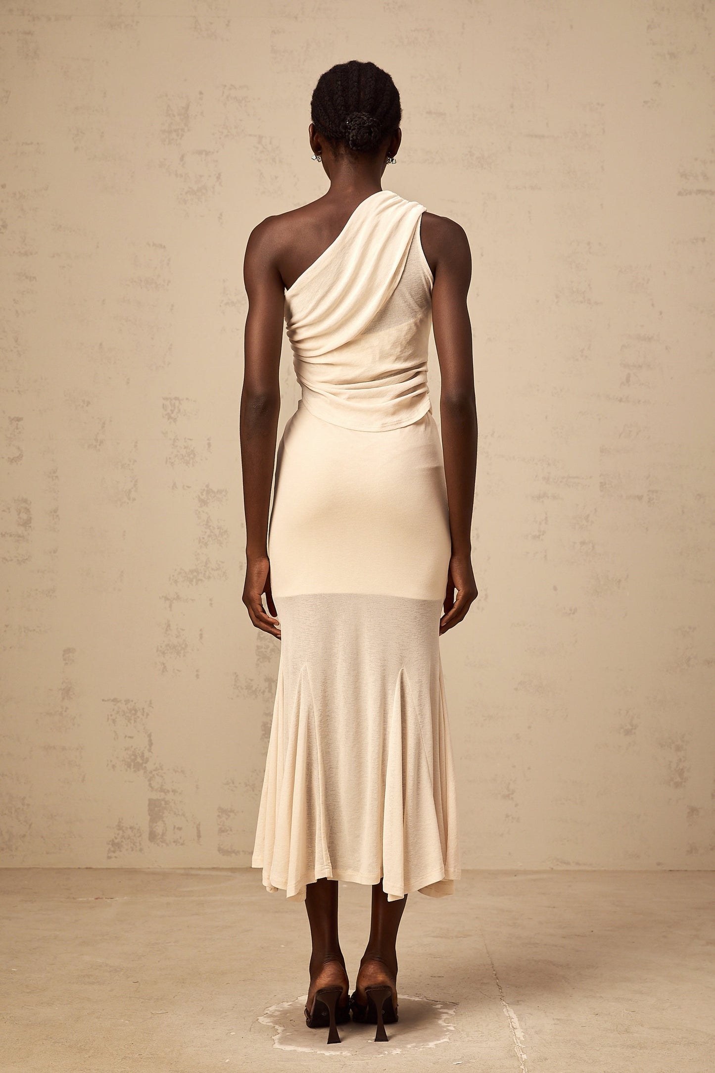 A woman wearing a neutralcolored matching set consisting of a stretch ruched top and skirt The top features long sleeves and the skirt has a formfitting silhouette Both pieces have a textured ruched design throughout