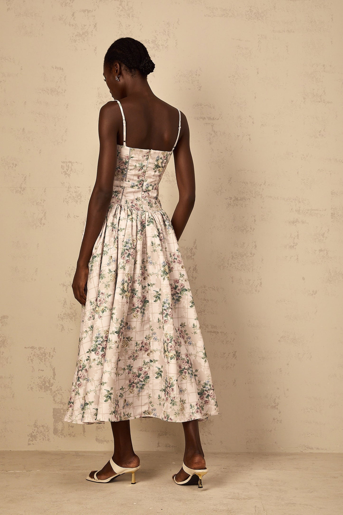 A woman wearing a neutralcolored midi dress with a delicate floral print pattern standing in a relaxed pose