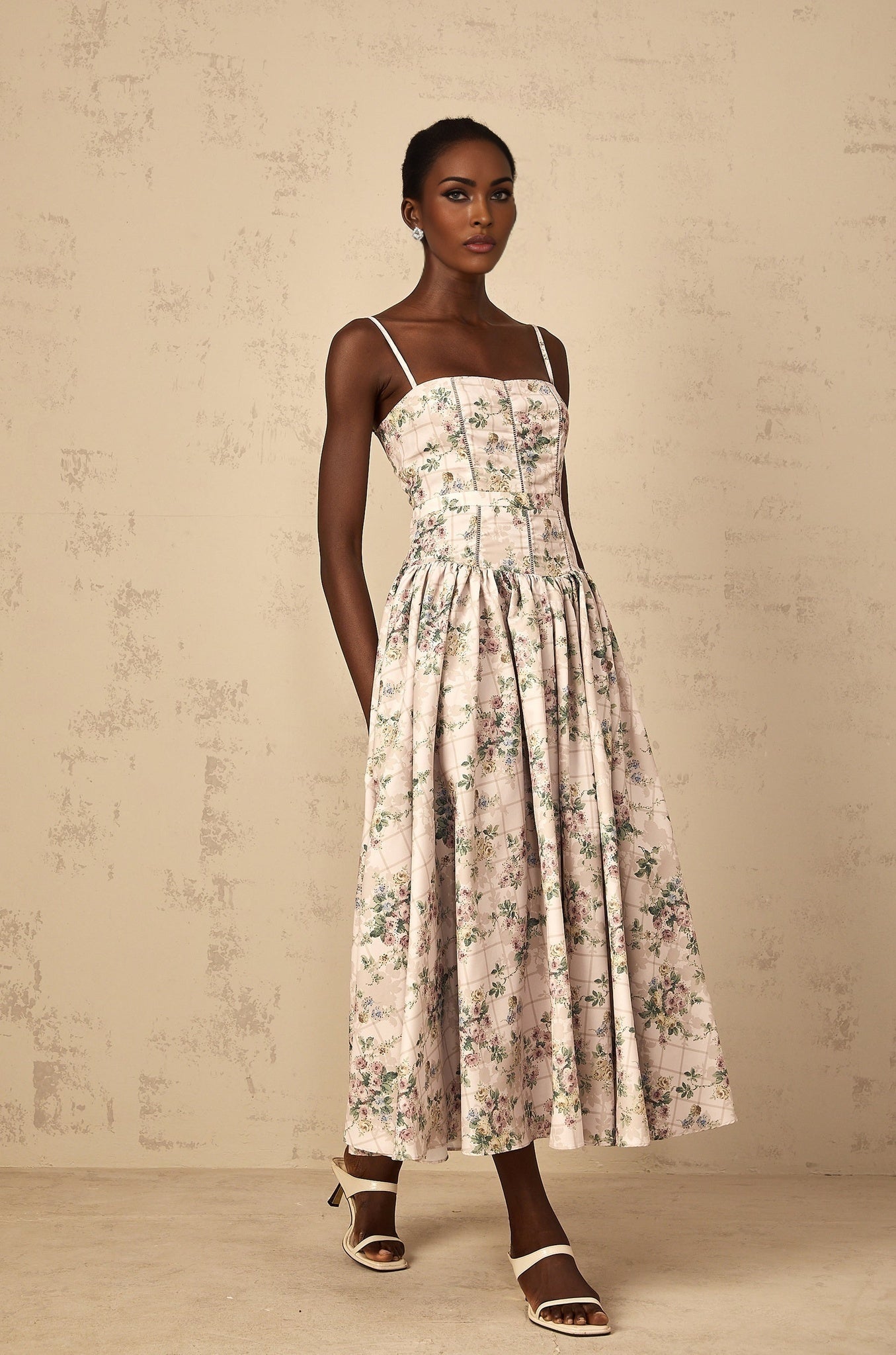 A woman wearing a neutralcolored midi dress with a delicate floral print pattern standing in a relaxed pose
