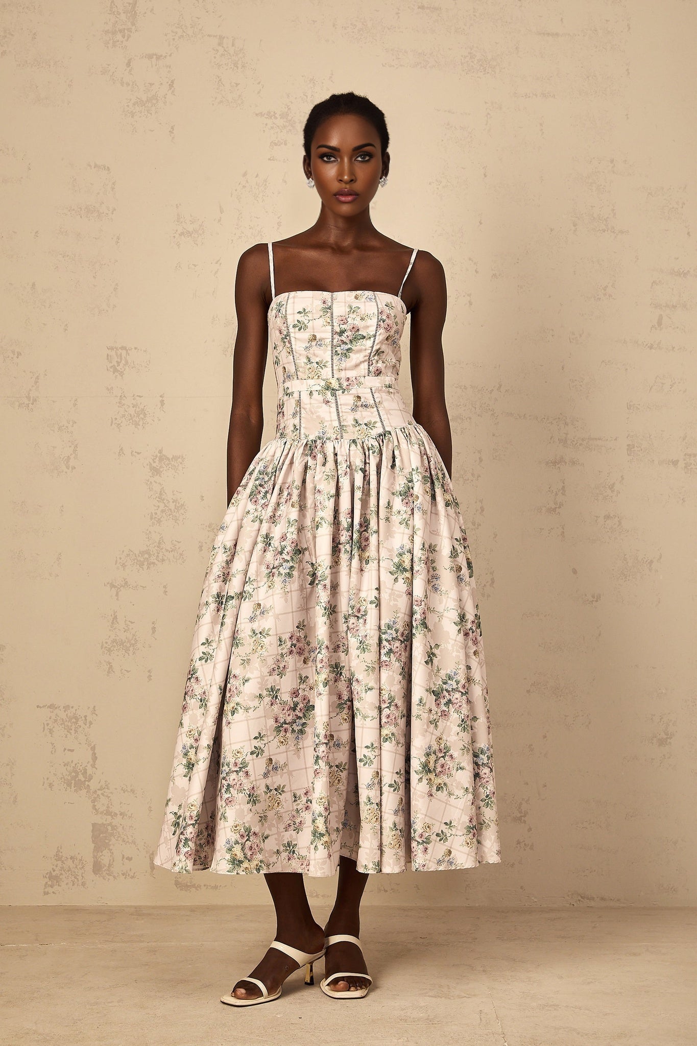 A woman wearing a neutralcolored midi dress with a delicate floral print pattern standing in a relaxed pose
