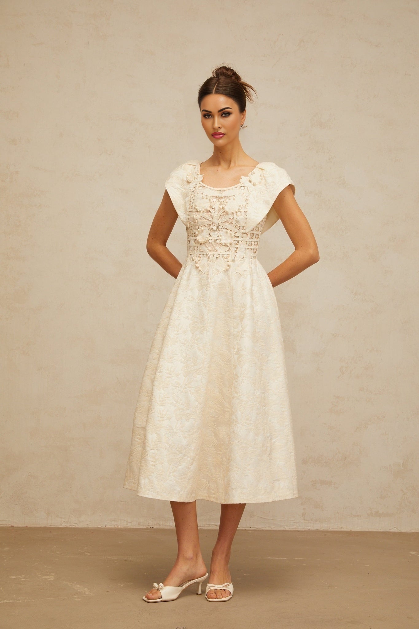 A woman wearing a neutralcolored midi dress with delicate floral embroidery and embellishments standing in a relaxed pose