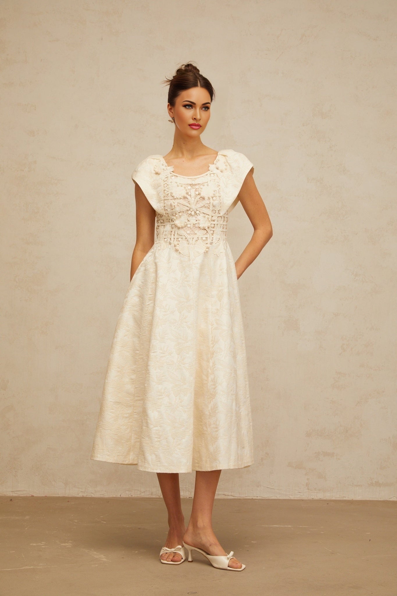 A woman wearing a neutralcolored midi dress with delicate floral embroidery and embellishments standing in a relaxed pose