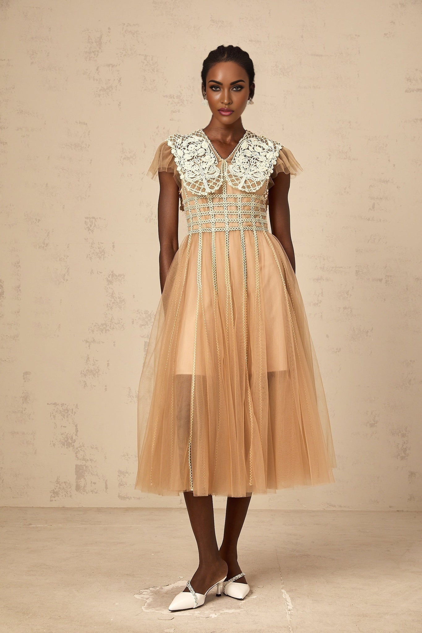A woman wearing a neutralcolored midi dress with lace panels and tulle detailing