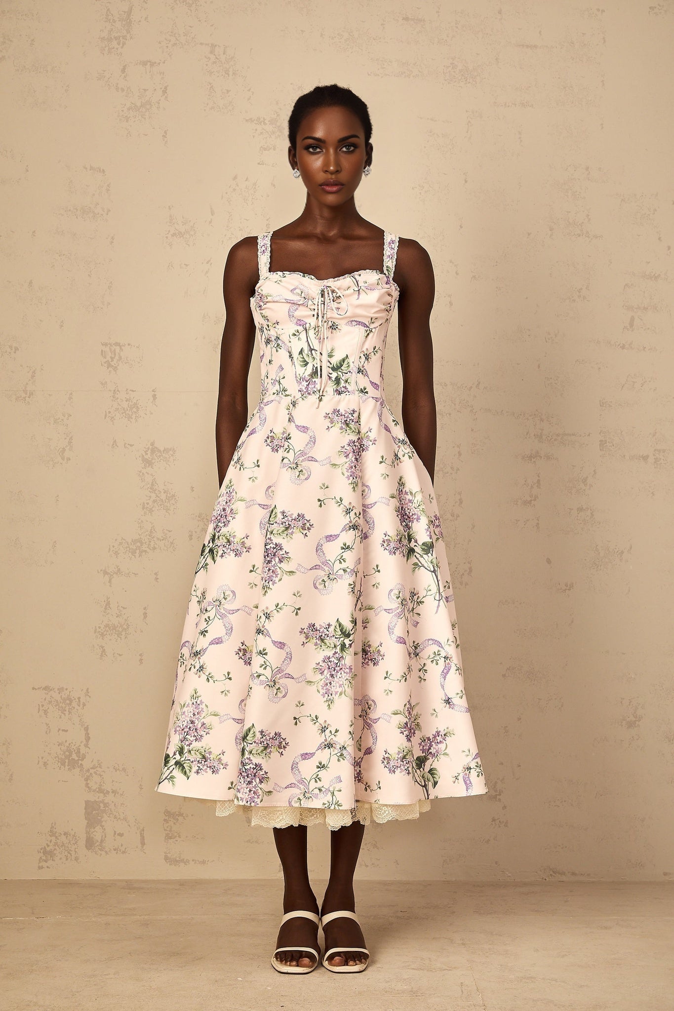 A woman wearing a pink midi dress with a floral print and shirred detailing