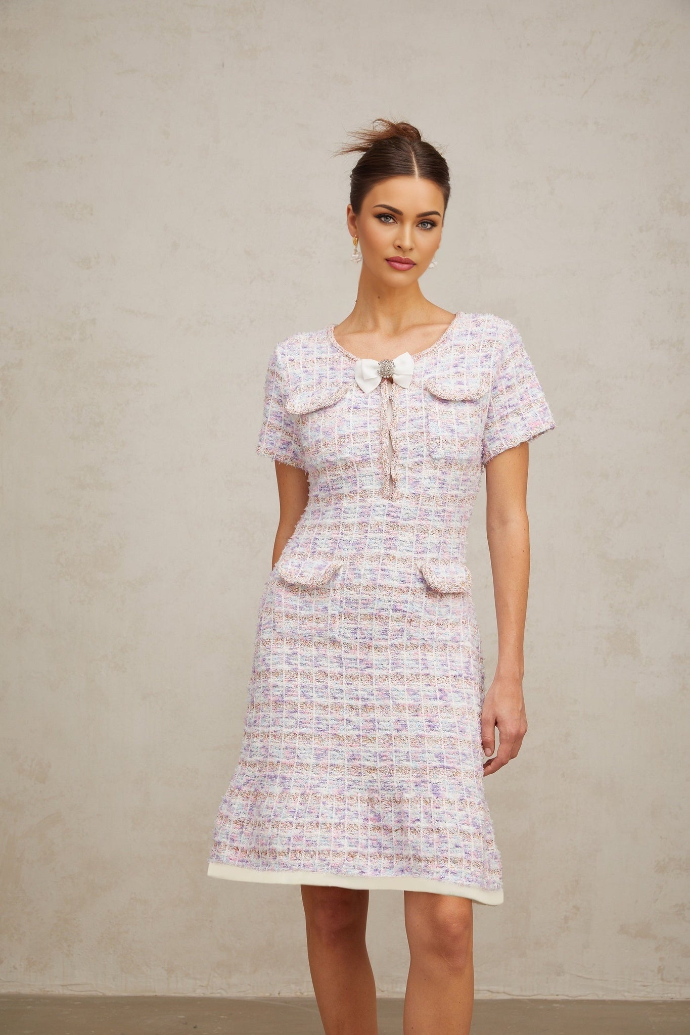 A woman wearing a purple and white checked knit midi dress with long sleeves and a fitted silhouette standing against a plain background