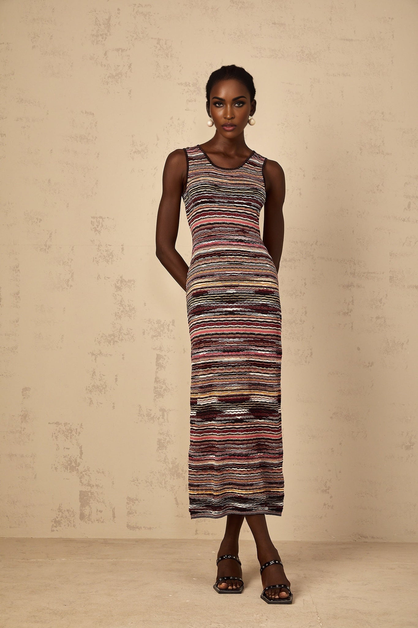 A woman wearing a purple striped crochet knit midi dress with long sleeves and a scoop neckline standing against a plain background