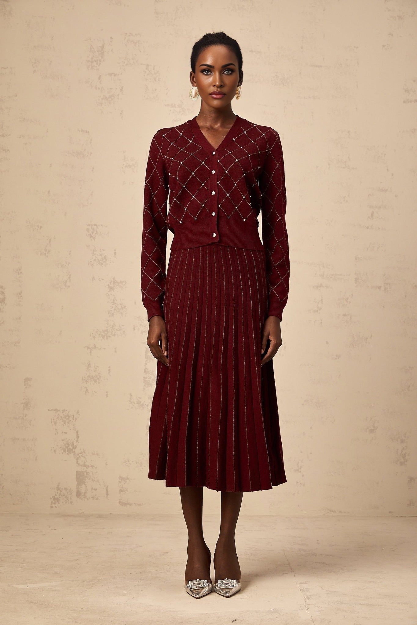 A woman wearing a red argyle knit cardigan and matching skirt set with embellishments The cardigan features an intarsia knit pattern and the outfit is styled as a coordinated ensemble