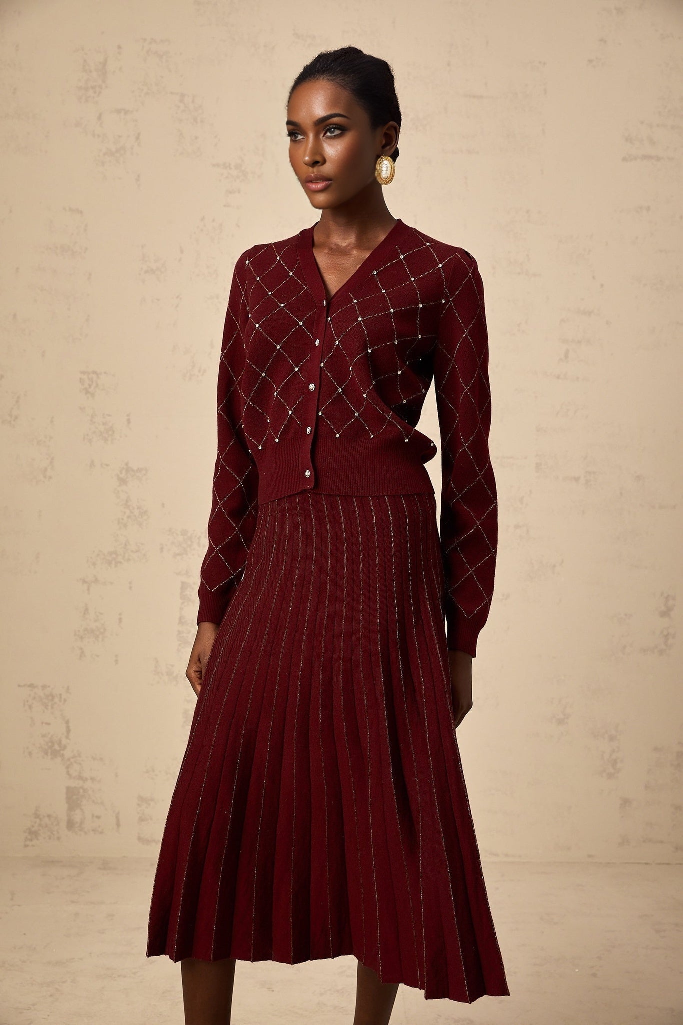 A woman wearing a red cardigan and matching skirt set with argyle pattern and embellishments The cardigan features intarsia knit design and the outfit is called Laurine