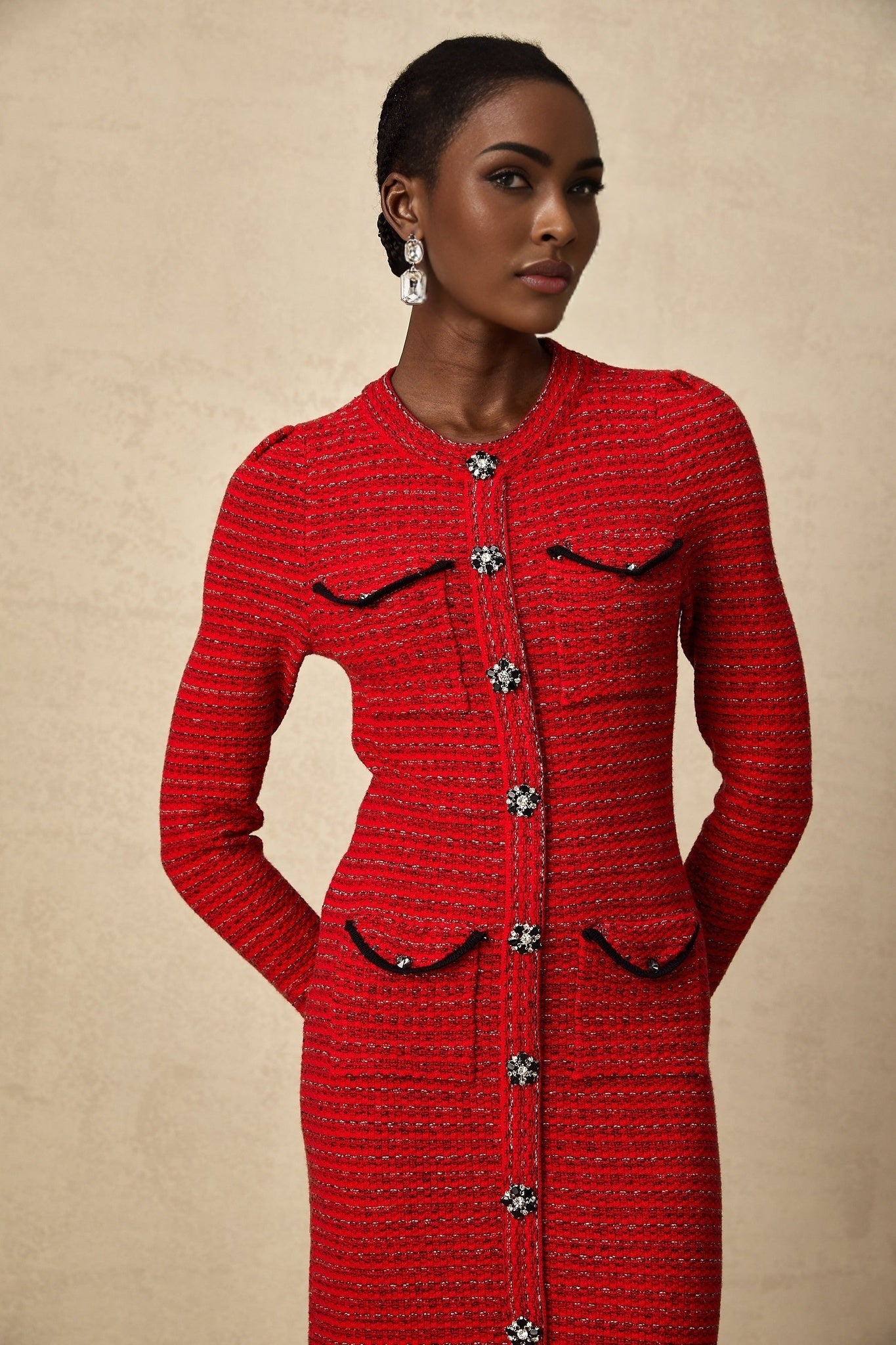 A woman wearing a red knitted midi dress with embellishments standing in a relaxed pose
