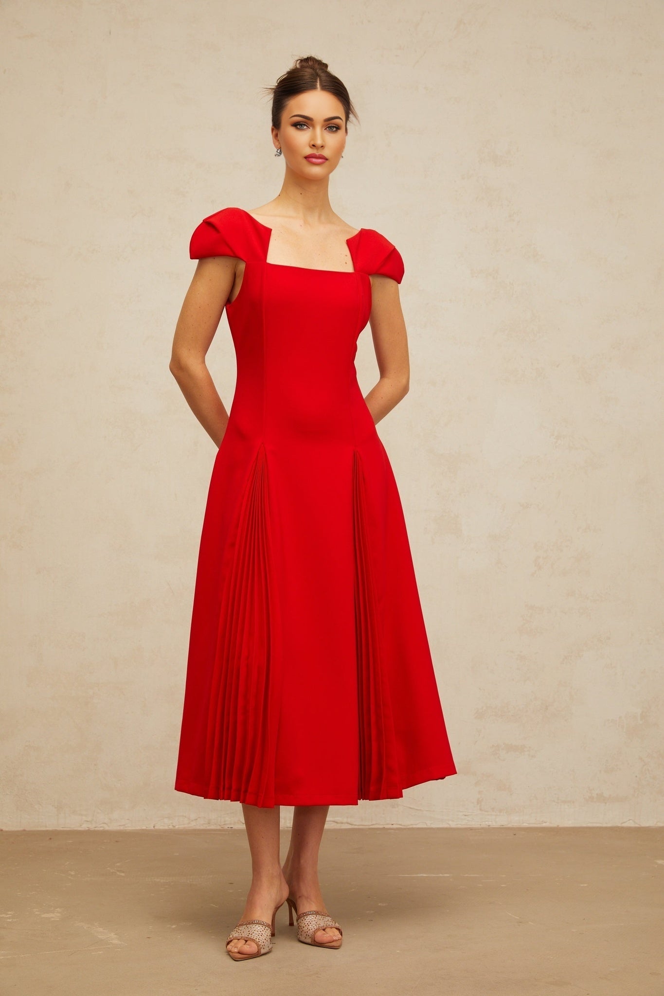 A woman wearing a red midi dress with pleated details and a flared skirt standing in a relaxed pose