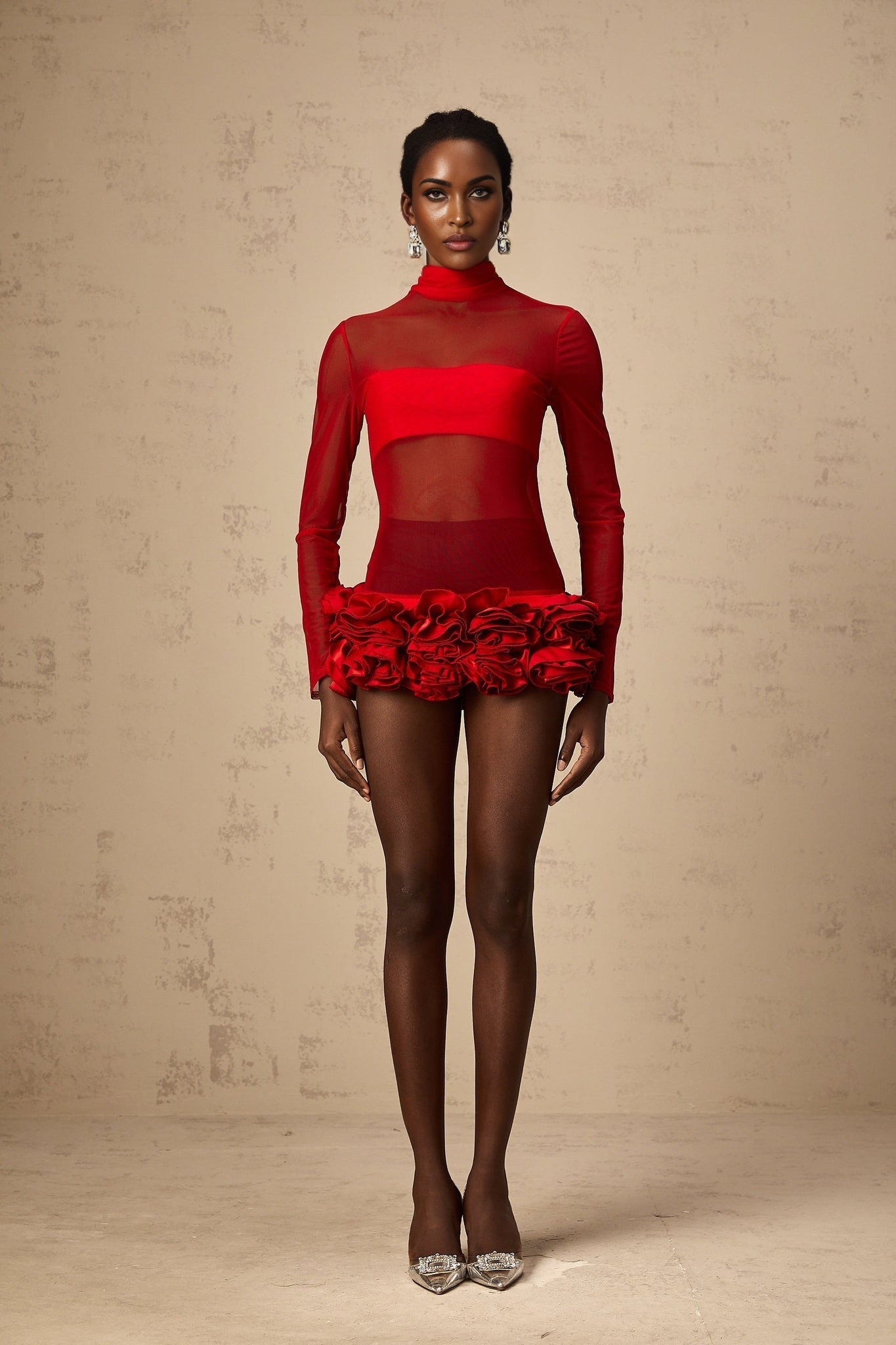 A woman wearing a red mini dress with 3d floral petal details made of semi sheer tulle fabric